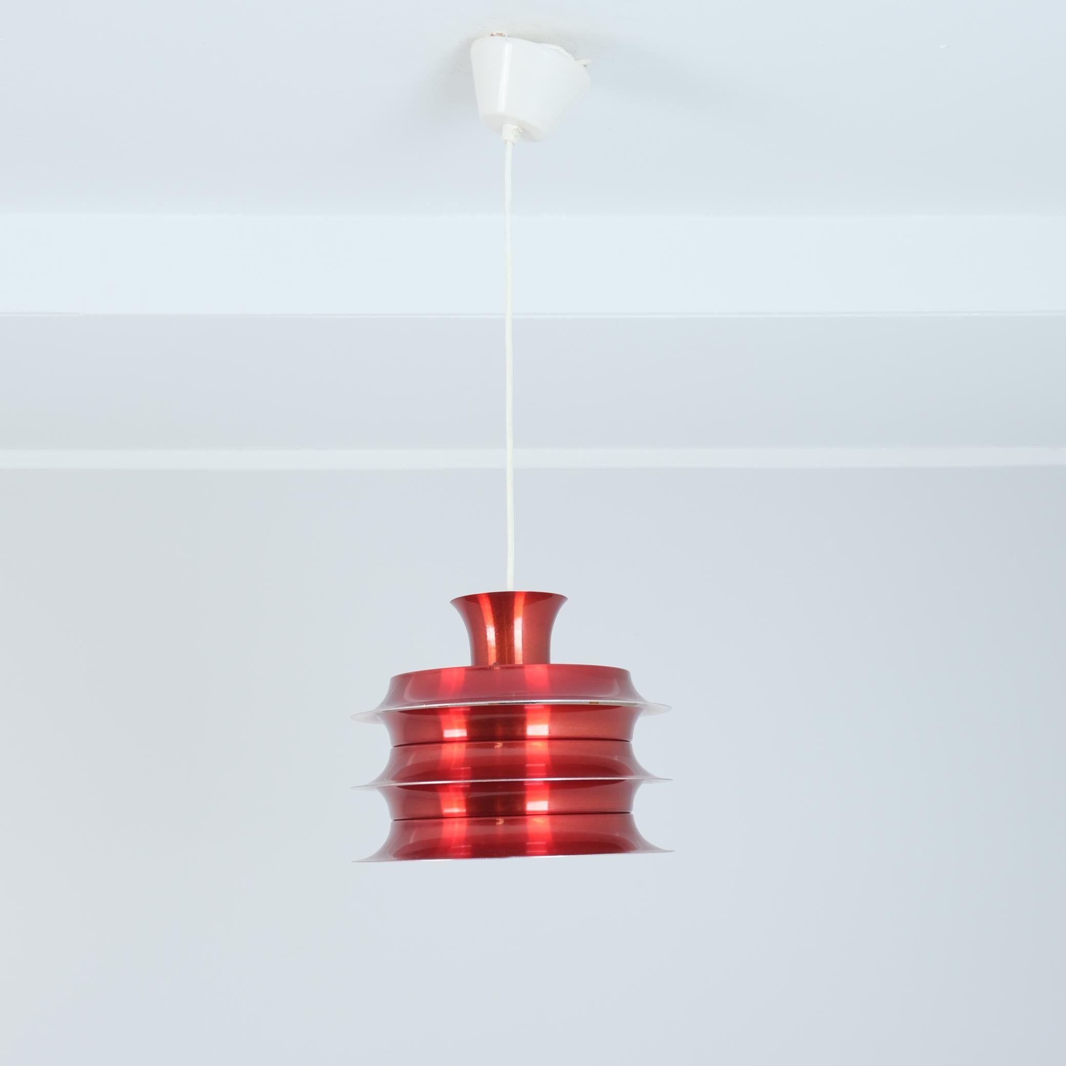 This vintage Scandinavian mid-century modern pendant lamp, showcases an iconic, layered design in a bold, glossy red finish. The lamp has a series of circular metal shades that are stacked with slight gaps between them, allowing for an eye-catching,