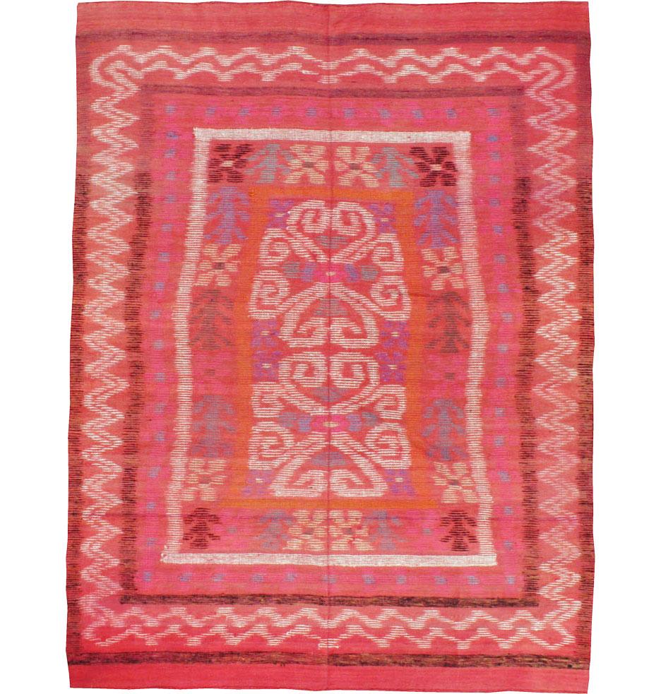 A vintage Finnish Kilim handmade during the mid-20th century in an accent rug size. The Scandinavian Modern design of abstract and geometric floral patterns and zigzags sits atop a primarily coral red field. A protective backing has been placed to