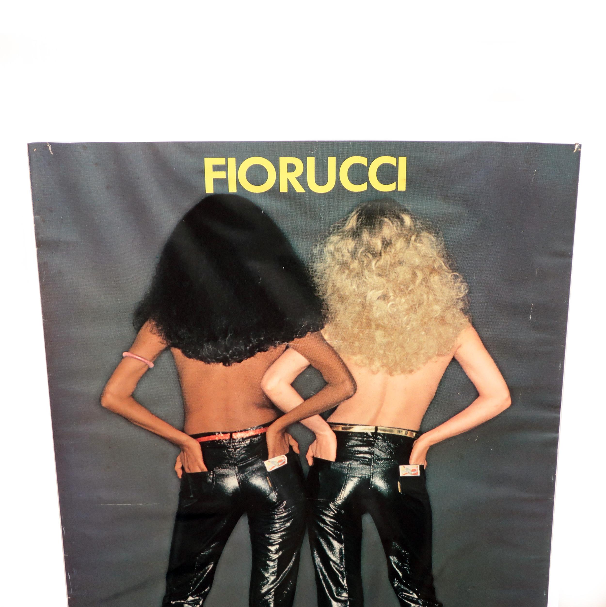 A vintage and rare Fiorucci poster with two women naked from the waist up wearing sparkly black pants and high heels. One model is Black with black hair and the other is white with blonde hair. Fiorucci branding appears in yellow at top center of
