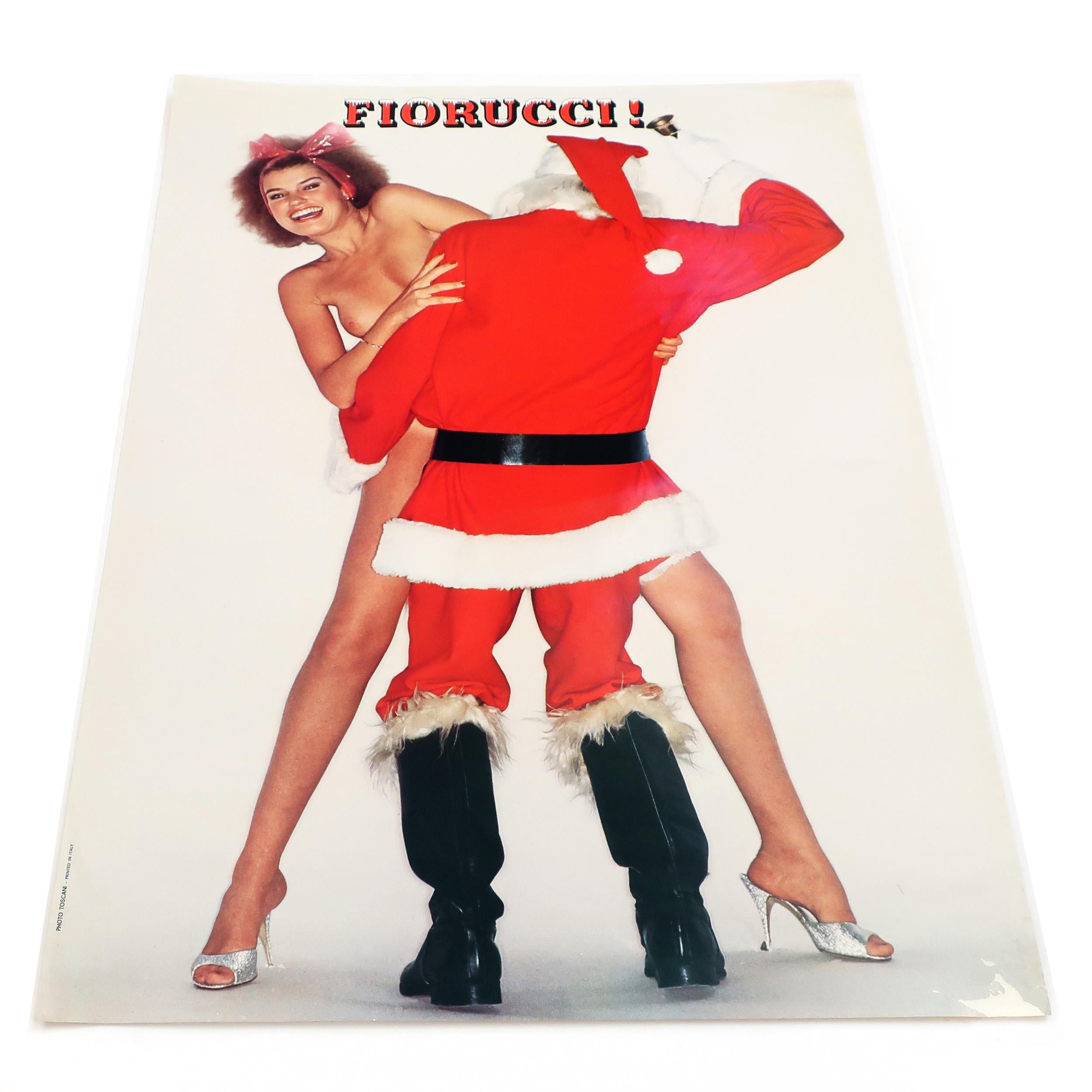 A vintage and rare Fiorucci poster capturing a naked model caught in the act of getting it on with Santa in full fur-lined suit with a little brass bell. The woman's hair is tied back with a pink ribbon and she’s wearing sparkly high heels, and