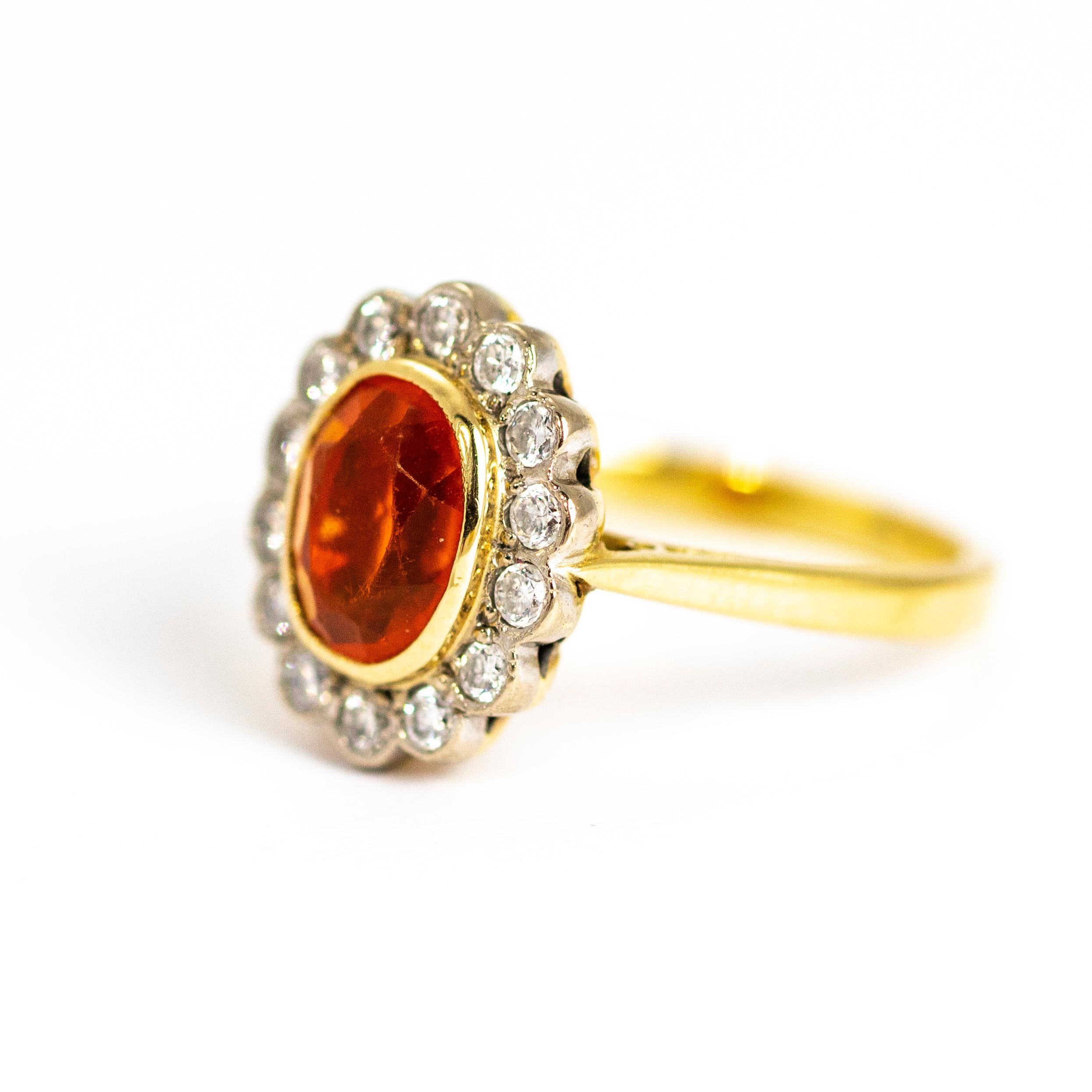 Fire opals are the most striking bright orange colour. This oval faceted stone is 7.3mm long and surrounded by beautiful and sparkling round brilliant cut diamonds all set in a charming cluster and sat upon a very simple gold band. It is believed