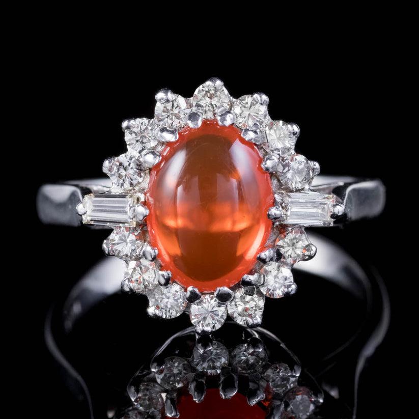 A spectacular vintage cluster ring crowned with a natural cabochon fire opal weighing approx. 1.75ct, haloed by fourteen bright brilliant cut diamonds and two baguette cuts.

The alluring opal displays a burning orange fire within and is