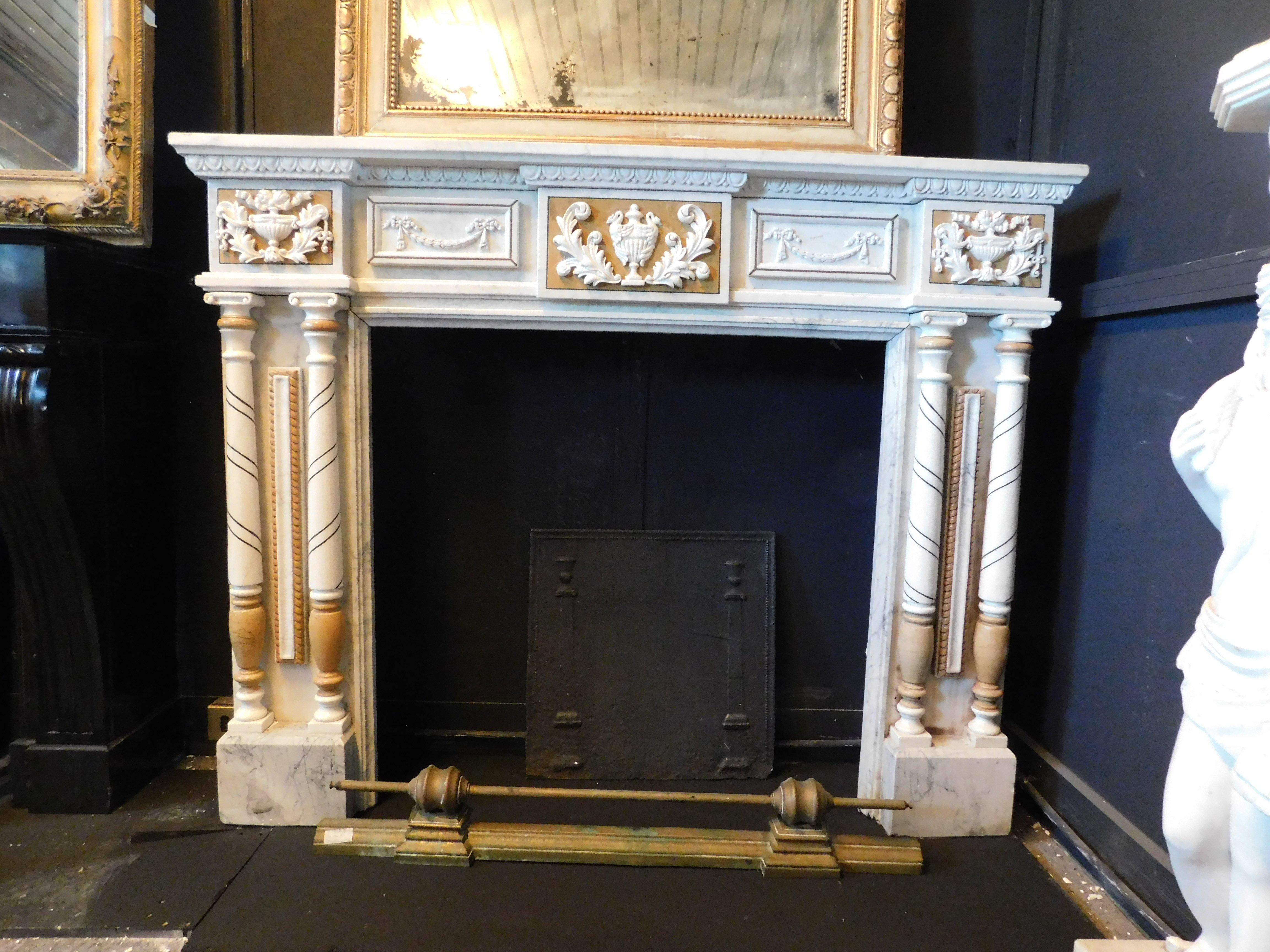 vintage fireplace in hand-carved white marble with yellow ocher inlays. Sides with turned columns and capitals, front with floral sculptures, cups and festoons. very particular coloring and elegant shape make it ideal for embellishing the furniture