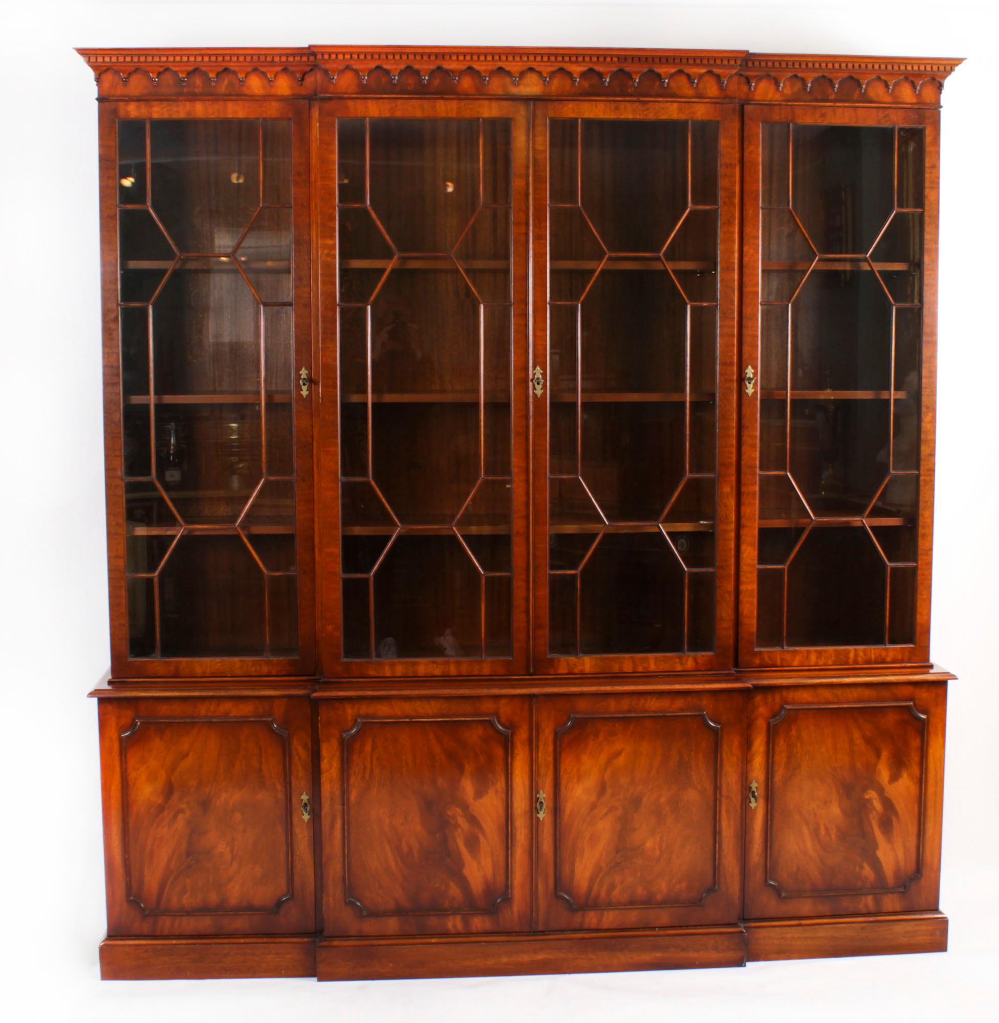 A delightful Vintage flame mahogany Georgian Revival library breakfront bookcase, dating from the mid 20th Century.

The top features a moulded cornice with a dental and arcaded frieze. The four astragal glazed doors open to reveal three adjustable