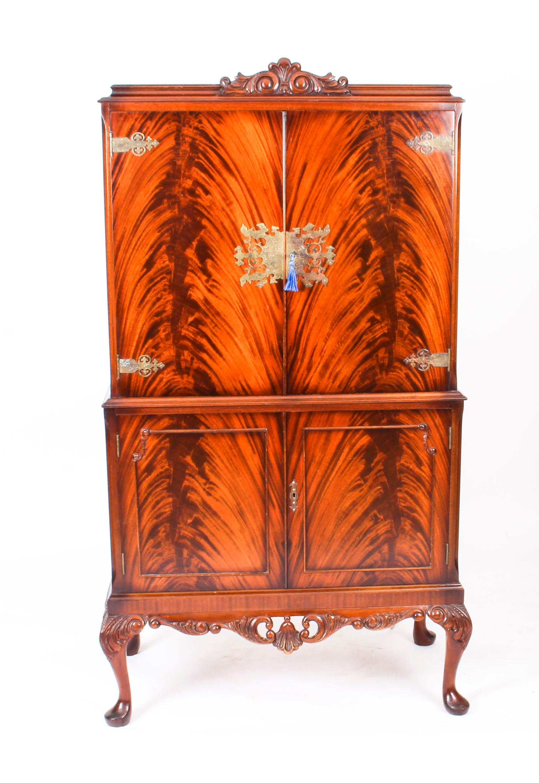This is a fantastic vintage flame mahogany cocktail cabinet with fitted and mirrored interior and brass mounts, dating from the mid 20th Century.

The upper part comprises a pair of doors that have beautiful small shelves with brass galleries on