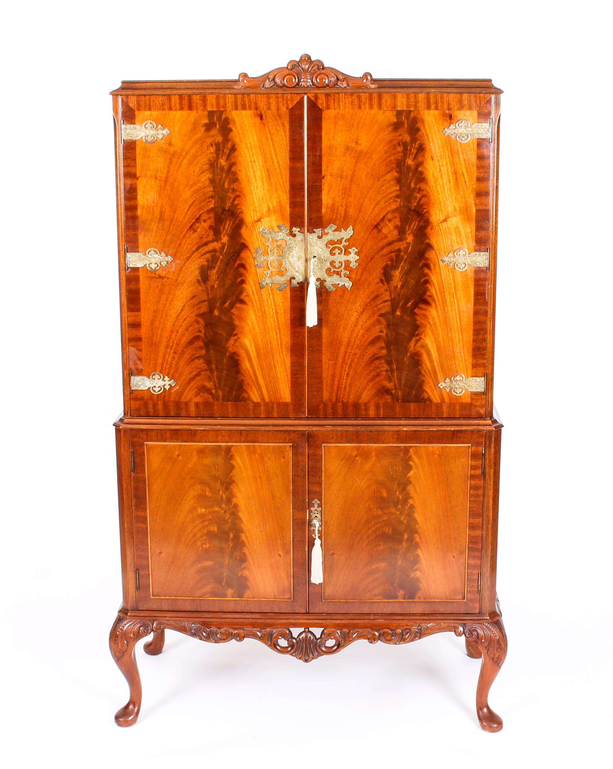 This is a fantastic vintage flame mahogany cocktail cabinet with fitted and mirrored interior and Ormolu mounts, dating from the mid-20th century.

The upper part comprises a pair of doors that have beautiful small shelves with brass galleries on