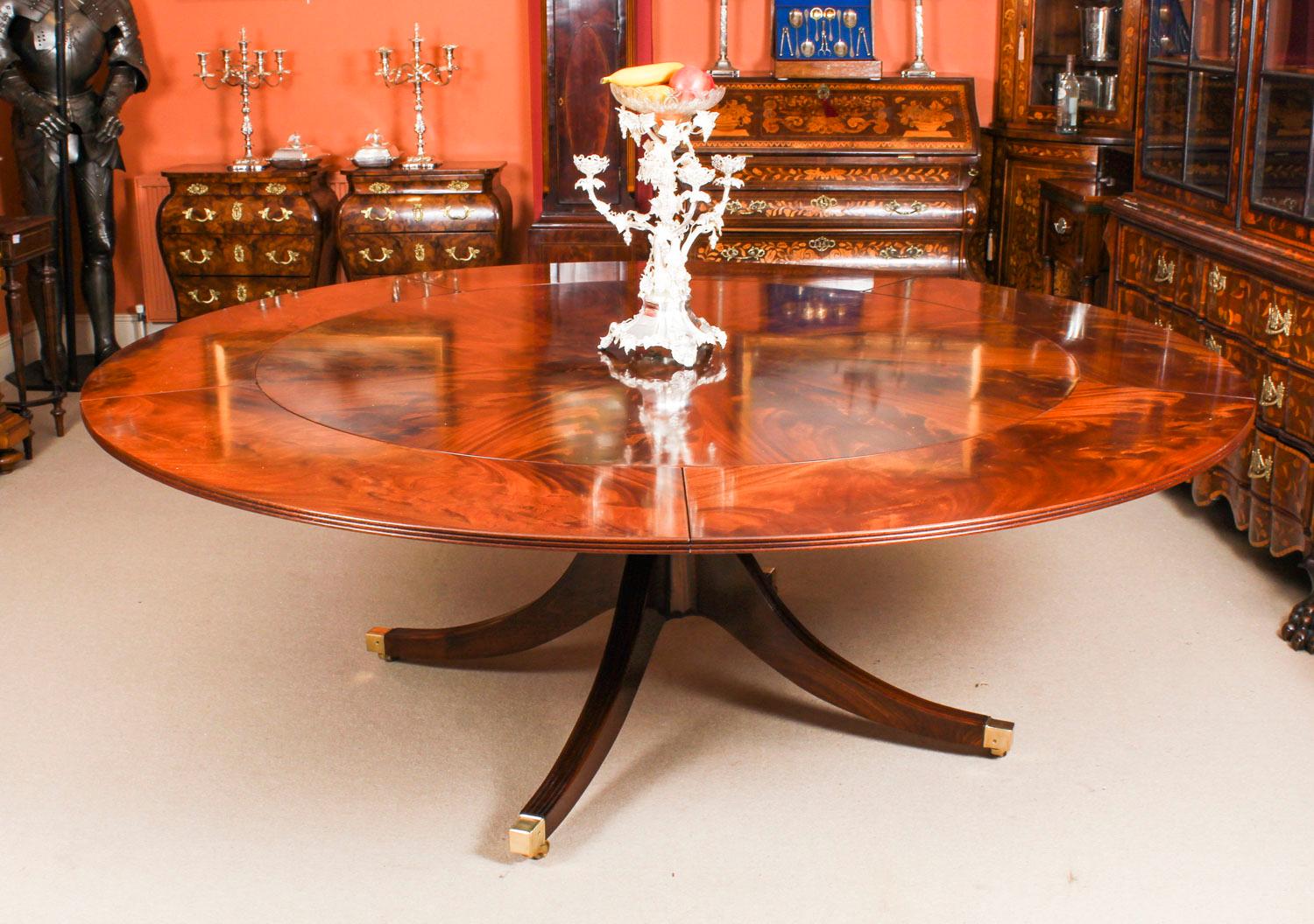 This is a beautiful Regency Revival Jupe style flame mahogany dining table, dating from the mid-20th century.

The table has a solid mahogany top that has five additional perimeter leaves that can be added around the circumference. It is very stable