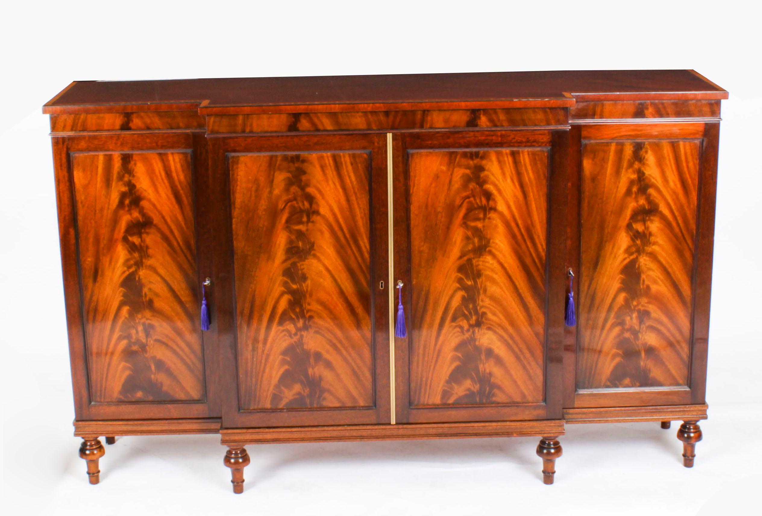 This is a fabulous Vintage Regency Revival breakfront sideboard by the master cabinet maker William Tillman, Circa 1980 in date.

It is made of stunning flame mahogany crossbanded in satinwood, fitted with four panelled doors and raised on turned