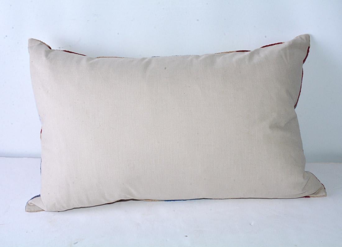 The vintage lumbar pillow is covered on the front with a flame stitch design in red, blue and beige chenille cotton. The back is of beige cotton. A zipper encloses an inner feather pillow. An accent for the sofa with character.