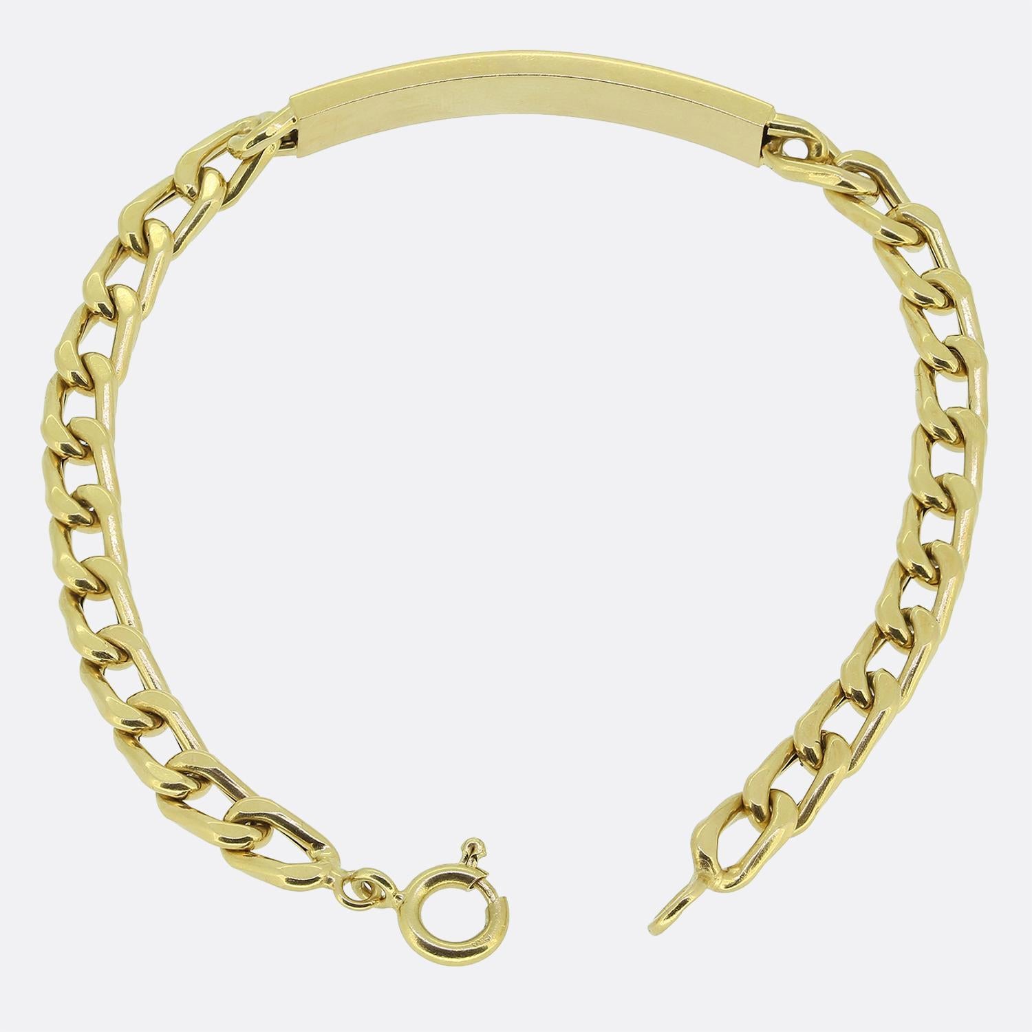 Aquí tenemos una pulsera de identificación clásica fabricada en oro amarillo de 18 ct. El diseño presenta una elegante barra pulida como pieza central, perfectamente integrada en medio de una serie de eslabones planos entrelazados con bordillos. A