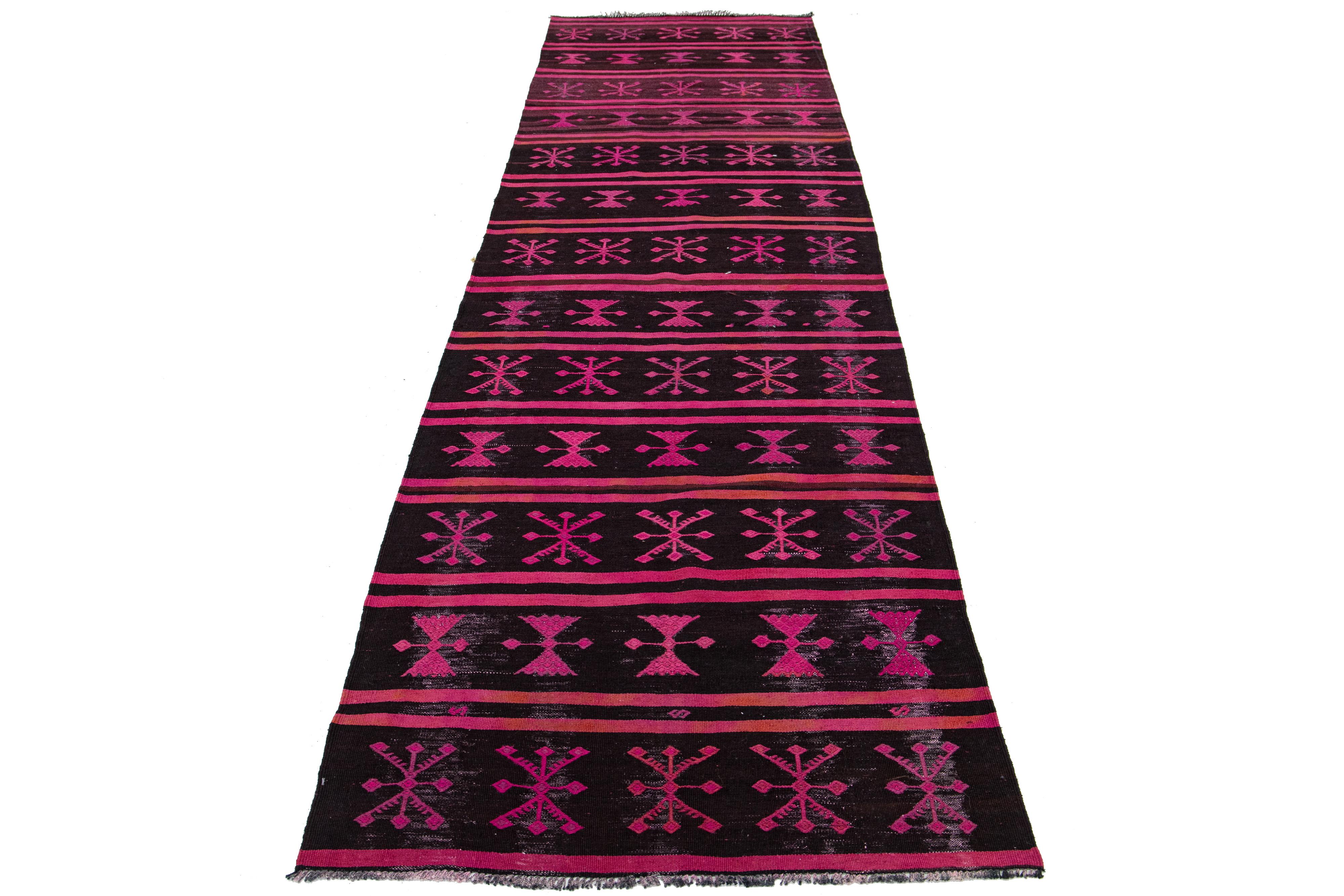 This is a handmade wool flatweave kilim rug with a dark brown field. The rug boasts an all-over geometric design in pink that adds to its aesthetic appeal.

This rug measures 3' x 11'.

Our rugs are professionally cleaned before shipping.