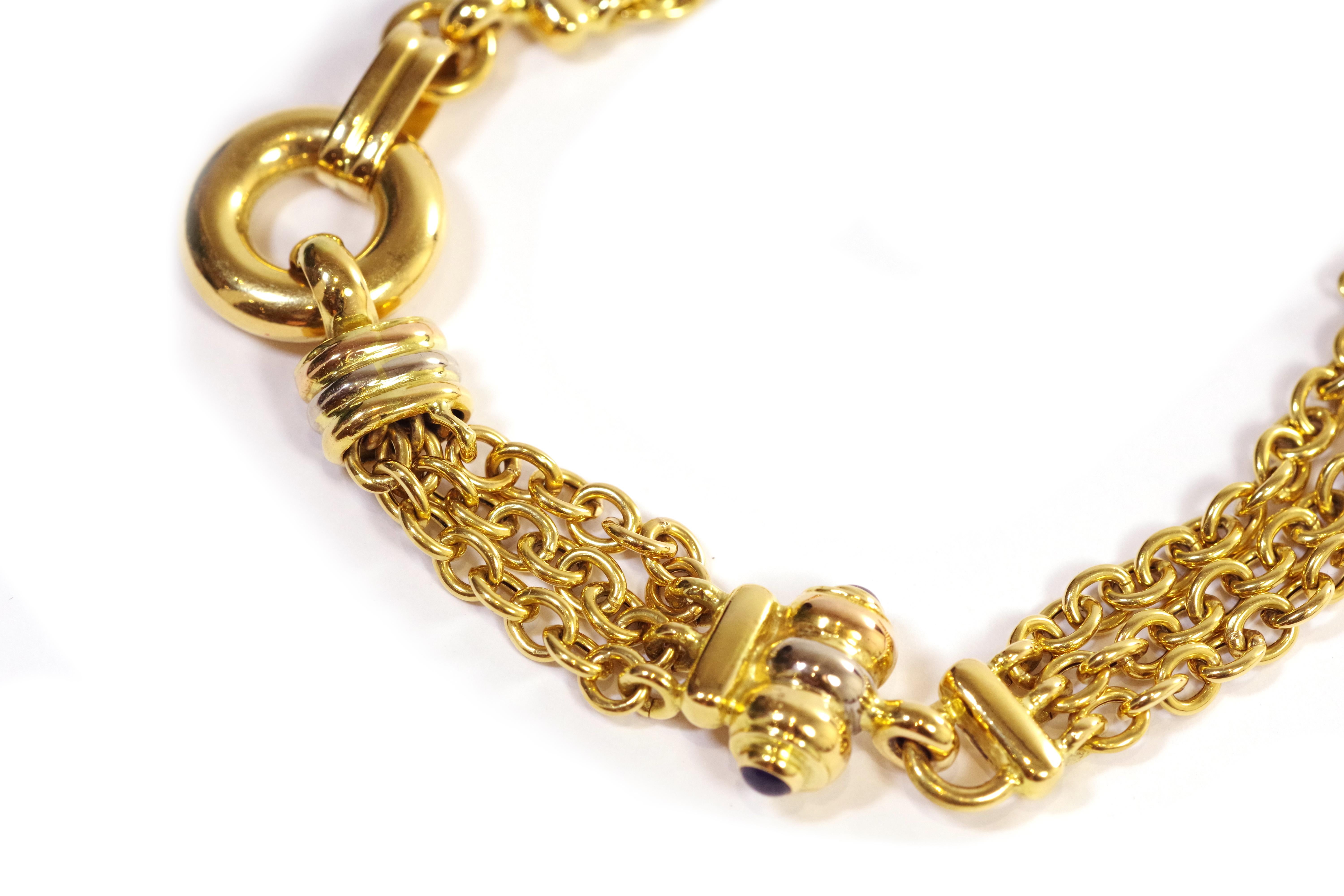 Vintage flexible bracelet in 18 karat yellow gold. The bracelet is composed of three rows of chains connected by tricolor gold elements. The piece is adorned with a setting of blue glass cabochons and a hollow gold ring. Created around 1990,