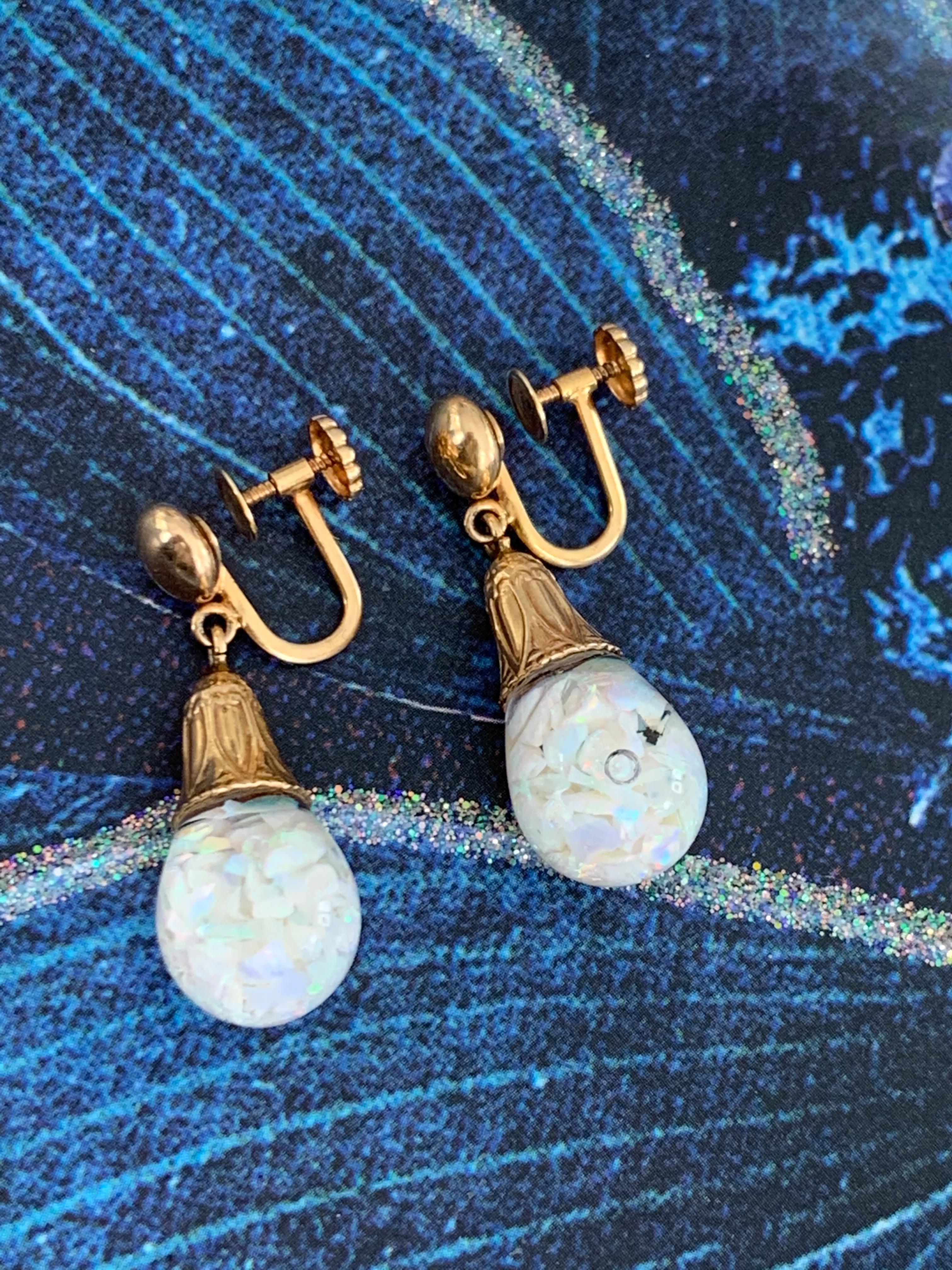 The drop in these vintage earrings feature floating, crushed Opal.  This unique way of presenting Opal, provides a reflection of beautiful color from all angles.  

The drop is capped with an engraved 14k yellow Gold setting and screw back