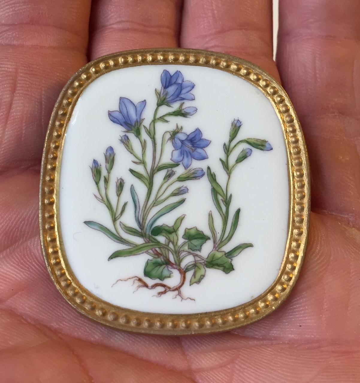 A Flora Danica brooch or pendant of porcelain, with gilded and sterling silver made by Anton Michelsen, and Royal Copenhagen, Denmark. Measures: H 4.8 cm. W 4.6 cm. Fully hallmarked to the backside.
