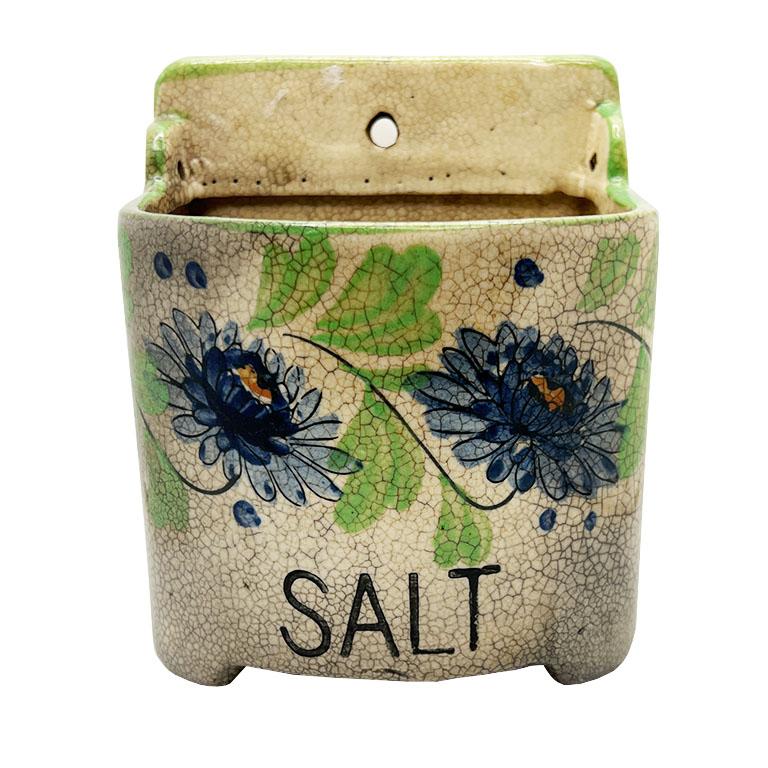 A mid-century ceramic hanging salt cellar with a floral motif. This fun salt vessel will be a great conversation piece in a kitchen! It is glazed in a creamy white and features a blue floral motif with lime green accents. The word 