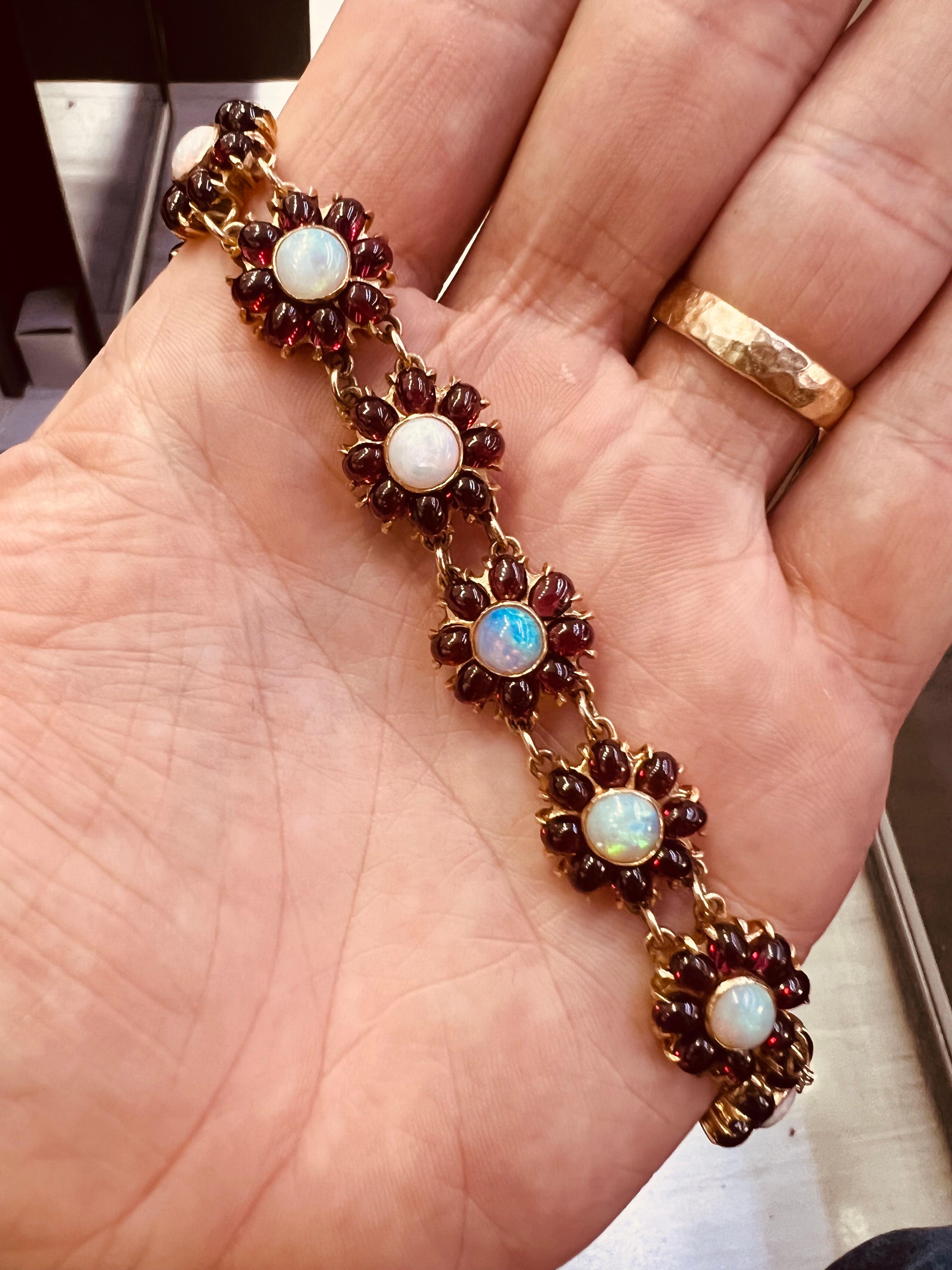One of a kind details seen in this vintage creation. This handmade bracelet is crafted in 14k yellow gold and set with garnet and opal gemstones throughout. The bracelet is crafted to resemble flowers, delicately set to be worn as wearable art work!