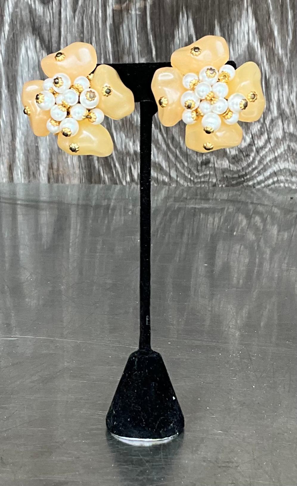 These Vintage Floral Lucite Pearl Clip-On Earrings feature intricate floral designs, often made from Lucite, a type of acrylic that has a smooth, polished surface. The flowers are typically delicately shaped with soft, curved petals, creating a