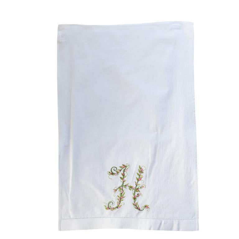 A pair of embroidered tea towels with a floral motif. Each towel features the letter 