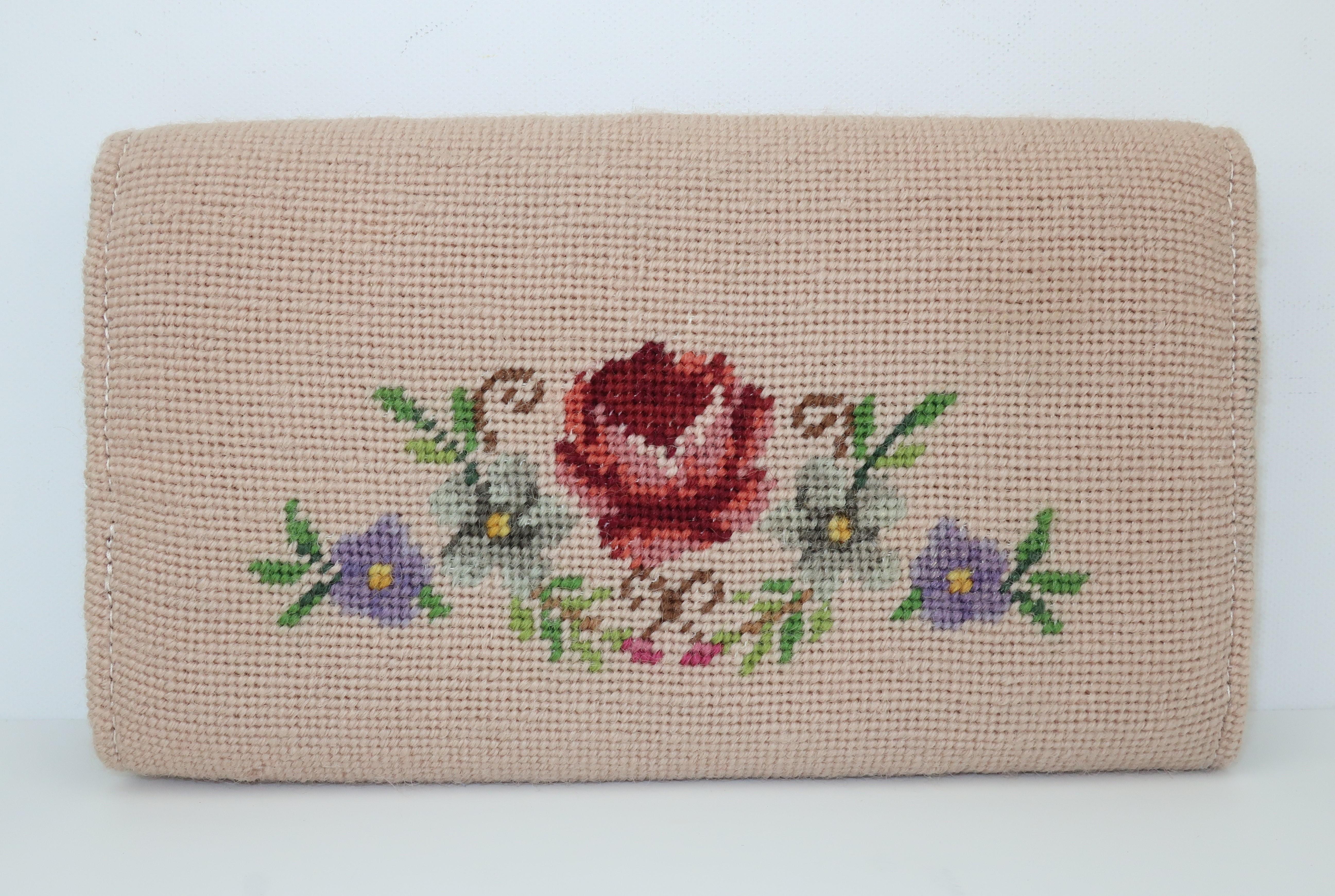 Accessorize an ensemble with this sweet floral needlepoint clutch handbag in shades of putty pink, green, yellow, brown, rose, burgundy, gray and lavender.  The fold over envelope style snaps open to reveal a brown fabric lined interior with an open