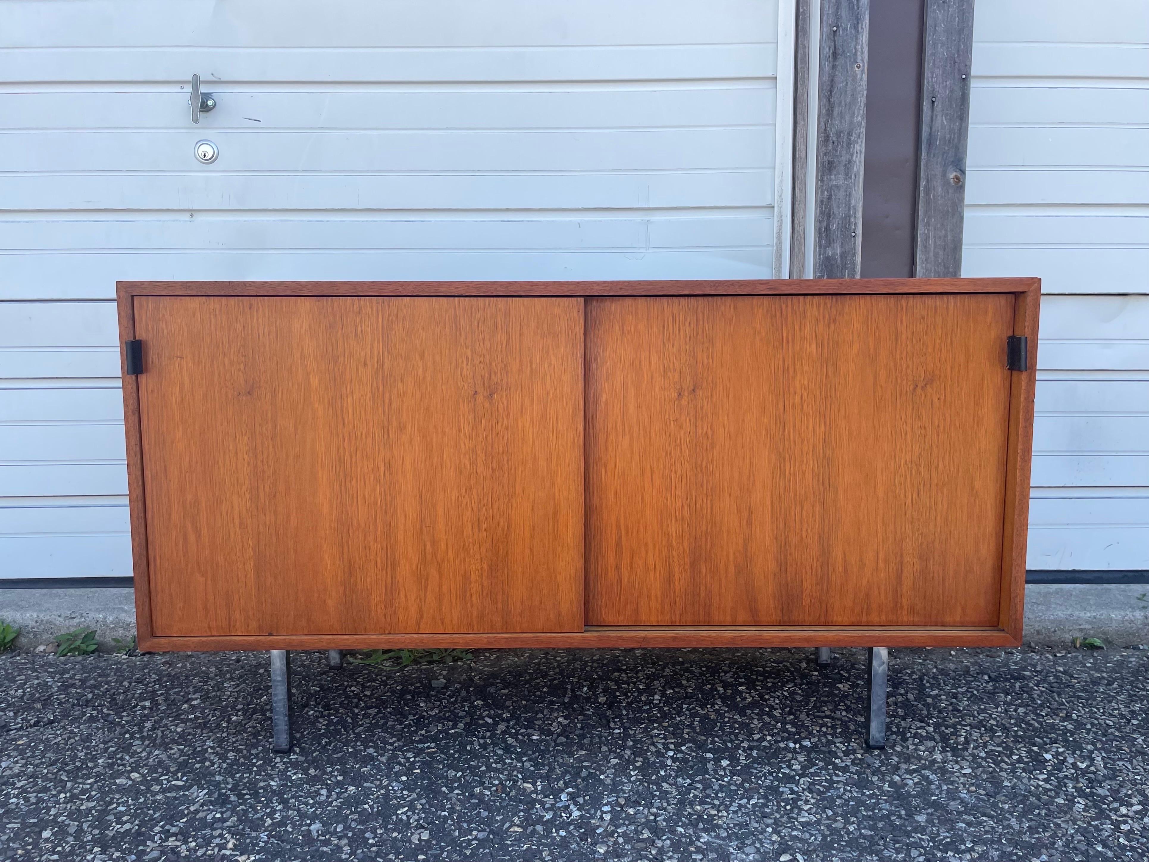 A classic 2 door cabinet in walnut with iconic black leather pulls and chrome legs. Designed by Florence Knoll, circa 1950s. 2 sliding doors and 4 adjustable shelves.