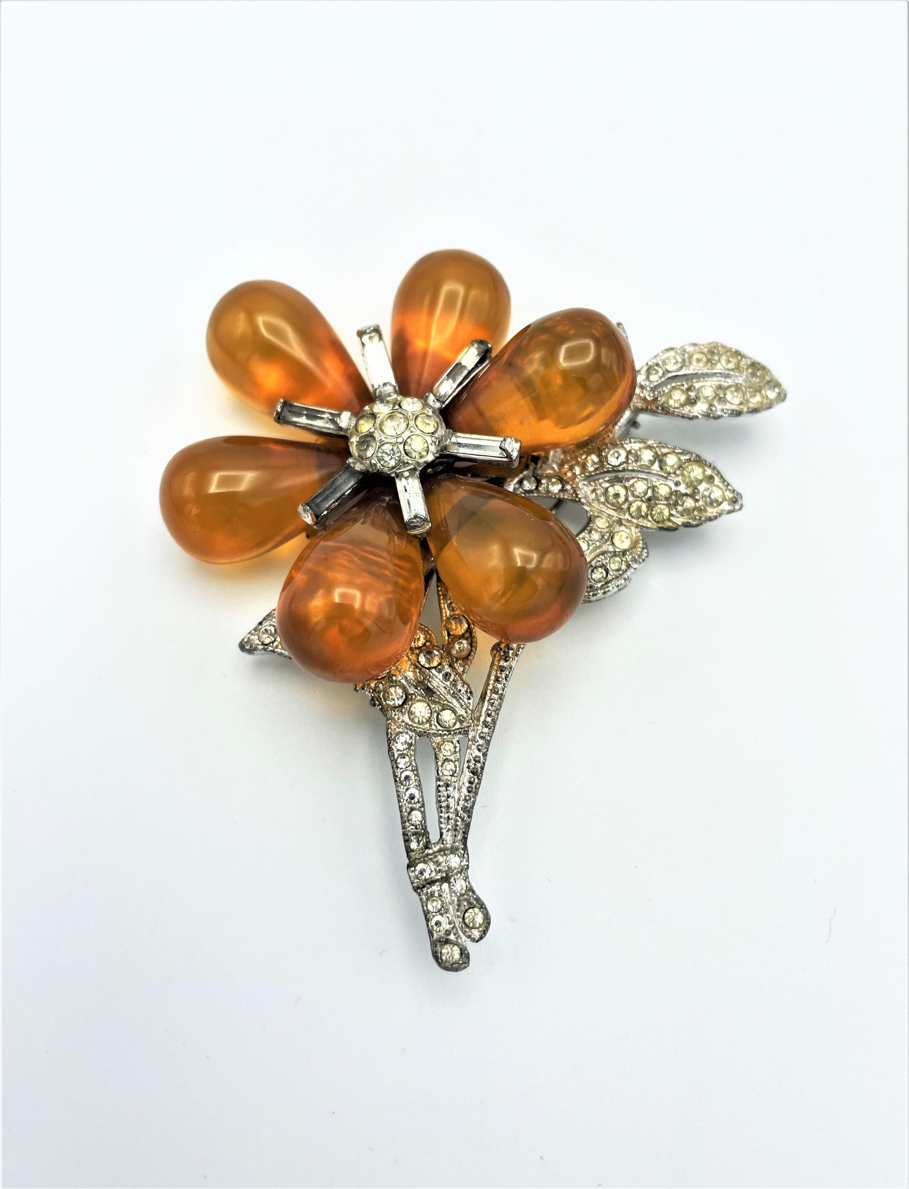 
A very unusual flower brooch from the early 1940s in the USA. The large flower consists of 6 transparent and  movable Bakelite drops. Pistils and leaves set with the finest rhinestones.
Measurement: Hight 7 cm, wide 6 cm, Bakelite drops 2 cm x 1