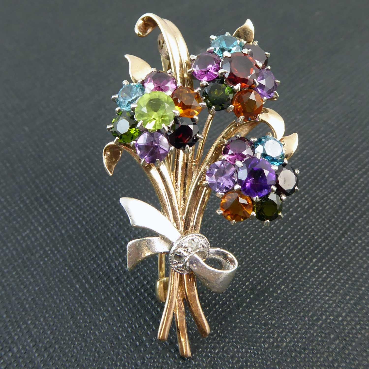 Vintage brooch in the form of a bouquet of flowers comprising three flower heads set with a mixture of semi-precious gemstones to include, period, garnet, amethyst, topaz and citrene.  The gem-set flowers are set against a background of yellow gold