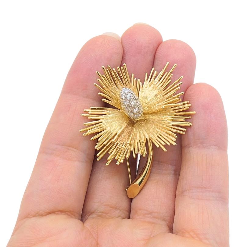 A vintage flower brooch 14k gold featuring diamonds.
The brooch’s layered petals are designed with a mix of radiating wires and broader brushed elements. The center is set with a small cluster of diamonds, nestled in an oval shape. This floral