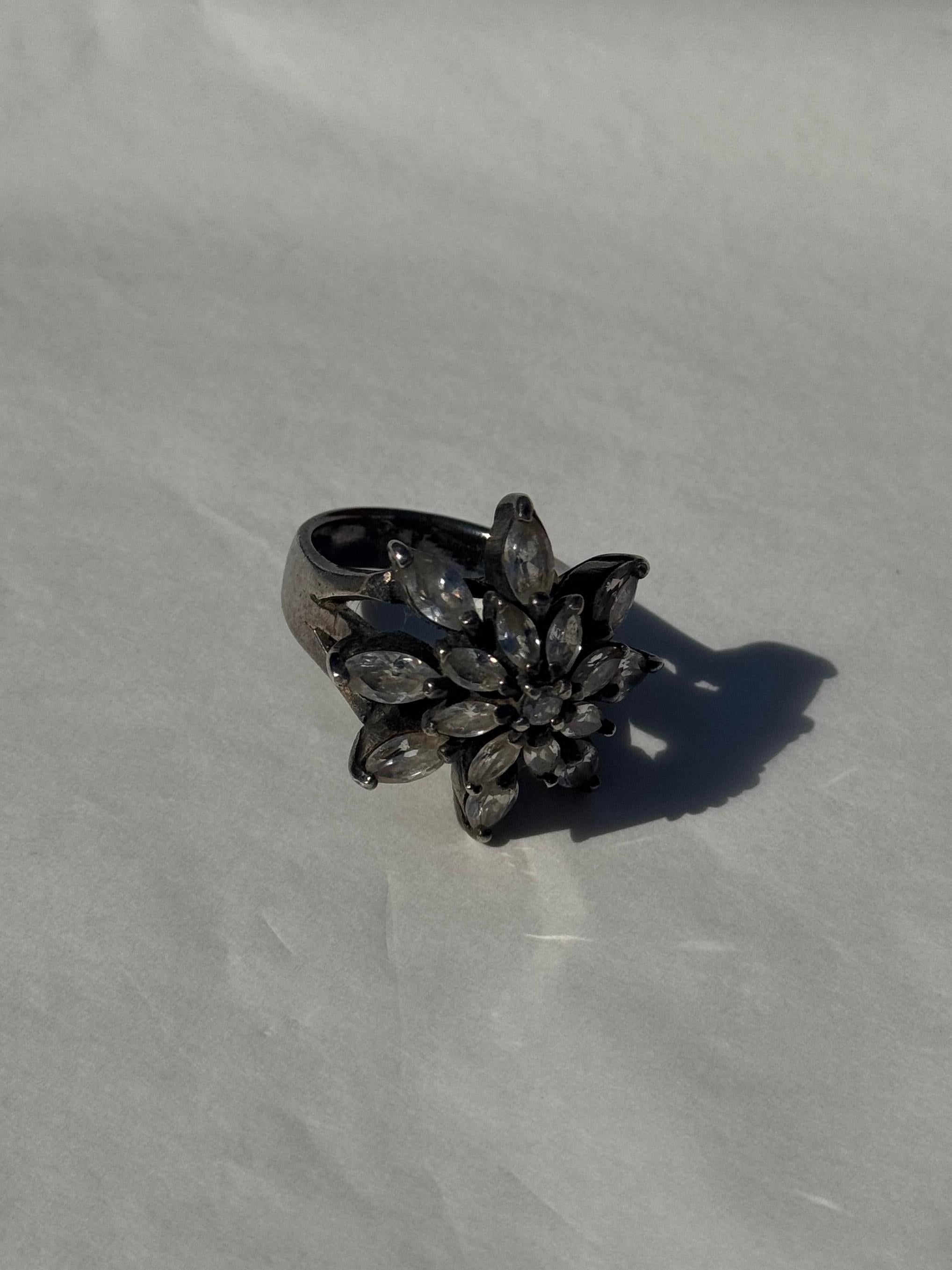 Cette élégante bague vintage, fabriquée en argent 925 véritable, date des années 1980, une décennie connue pour ses bijoux audacieux et expressifs. Le motif floral est composé de cristaux clairs, chacun taillé en forme de pétale allongé et disposé