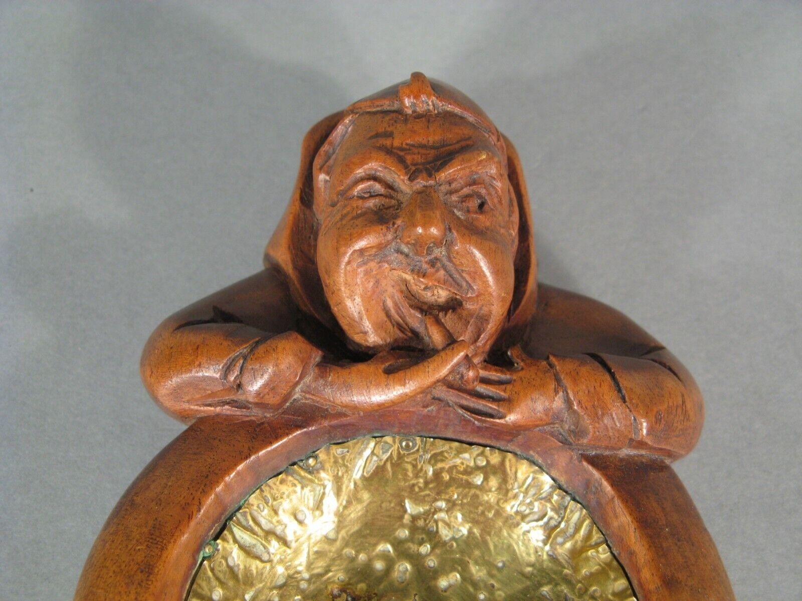 This exquisite ashtray, crafted from carved and patinated wood, features a charming design of a monk's head enjoying a cigar. A true piece of folk art, this ashtray showcases intricate craftsmanship from the early 20th century. The interior and
