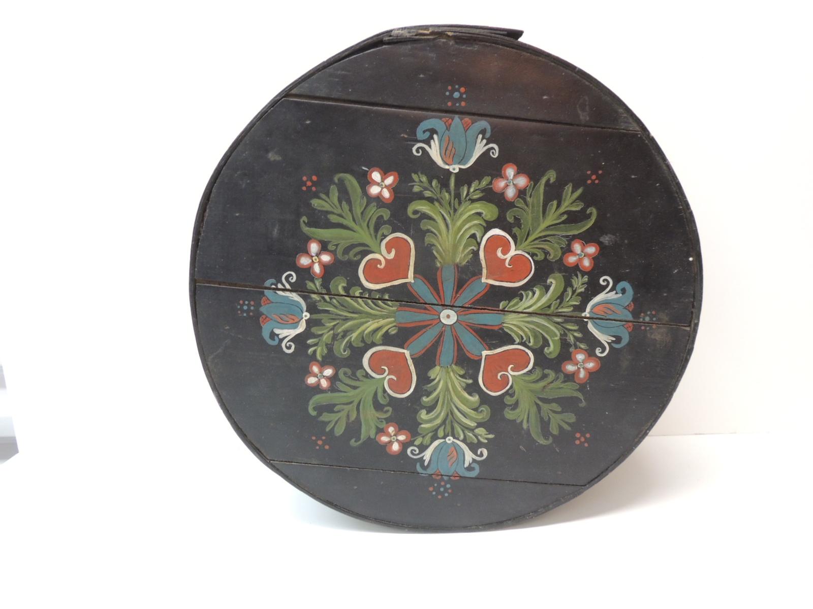 Folk Art hand painted round box
(Originally a cheese box)
Black mate paint with floral and heart motifs on the top and floral bouquets all around the box.
Palette in shades of blue, white, red, hunter green and black
Size: 15