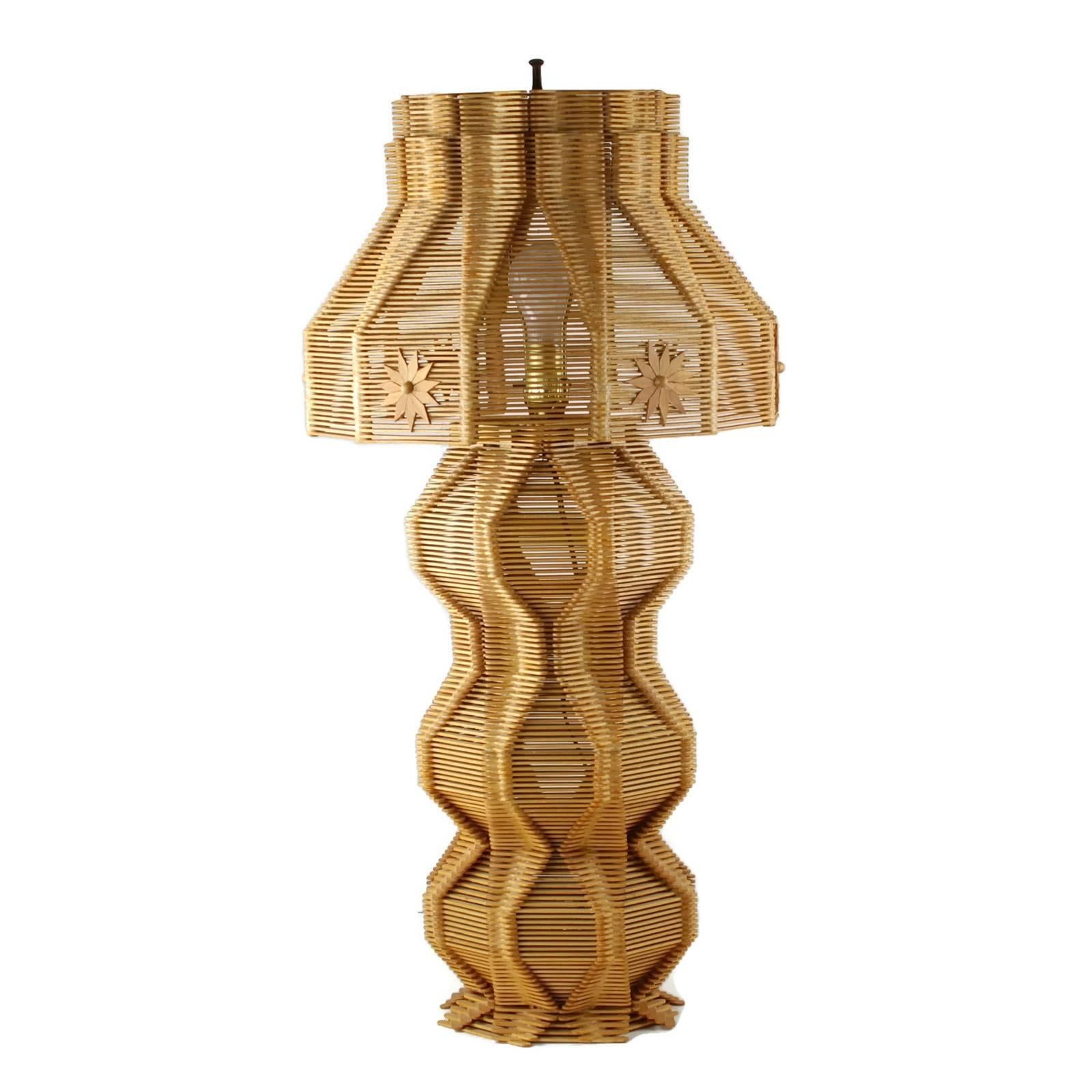 This large handmade Folk Art table lamp and matched shade are composed of popsicle sticks which have been arranged in a highly detailed geometric pattern. The lamp base has a sculptural quality with three ovoid sections located atop an octagonal