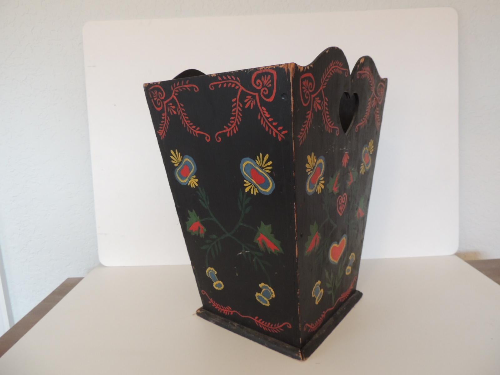 Vintage Folk Art style Wastebasket or umbrella stand.
Primitive painted bin with heart motif cutout handles.  Artisanal piece.
Hand painted on all four sides in shades of red, green, yellow and black.
Nice patina and floral pattern,
Size: 11' D x