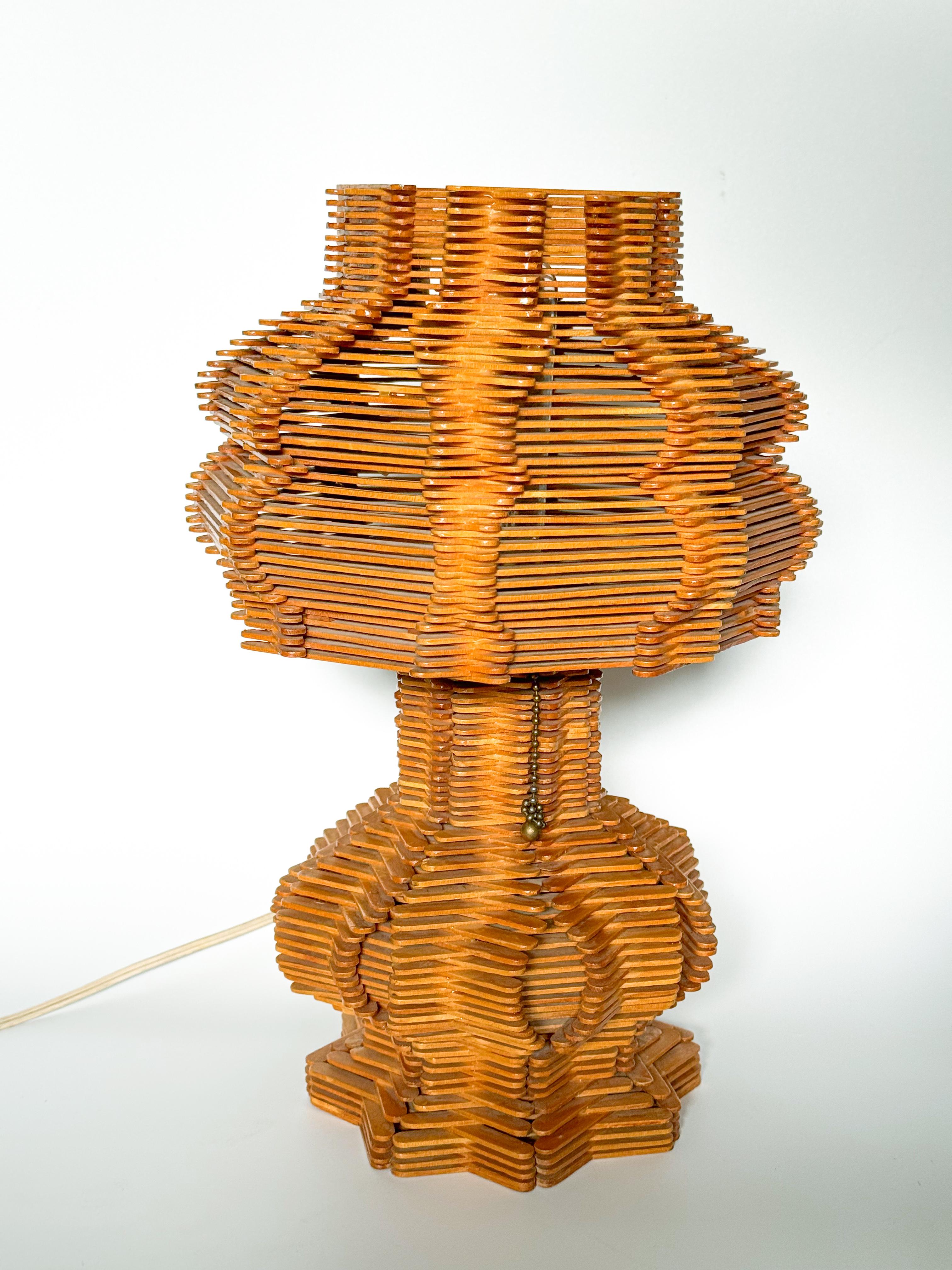 This captivating midcentury Folk Art table lamp is a remarkable representation of the post-war American hobby and craft movement. Handcrafted entirely from meticulously arranged popsicle sticks, the lamp showcases an intricate geometric design that