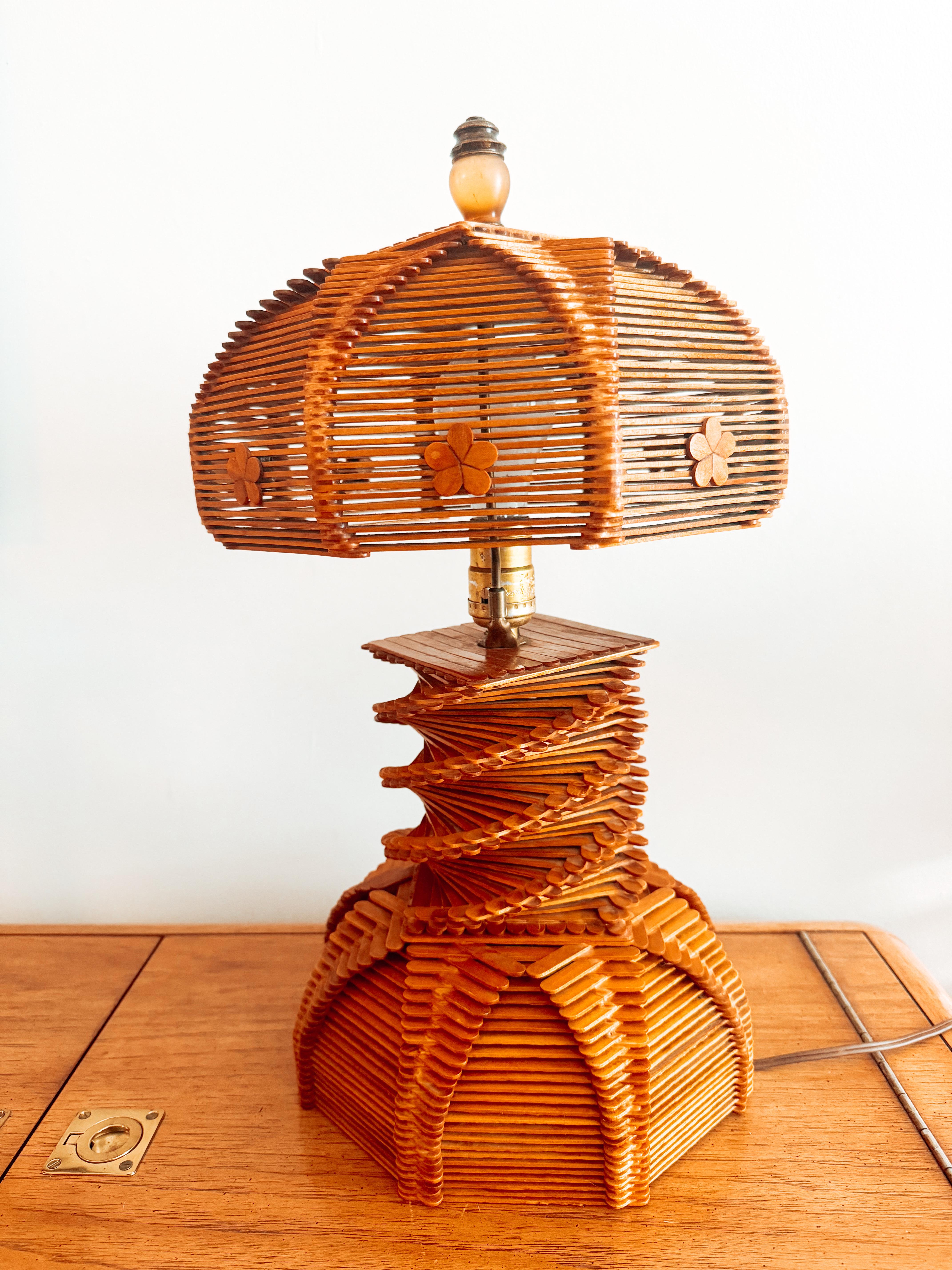 This captivating midcentury Folk Art table lamp is a remarkable representation of the post-war American hobby and craft movement. Handcrafted entirely from meticulously arranged popsicle sticks, the lamp showcases an intricate geometric design that