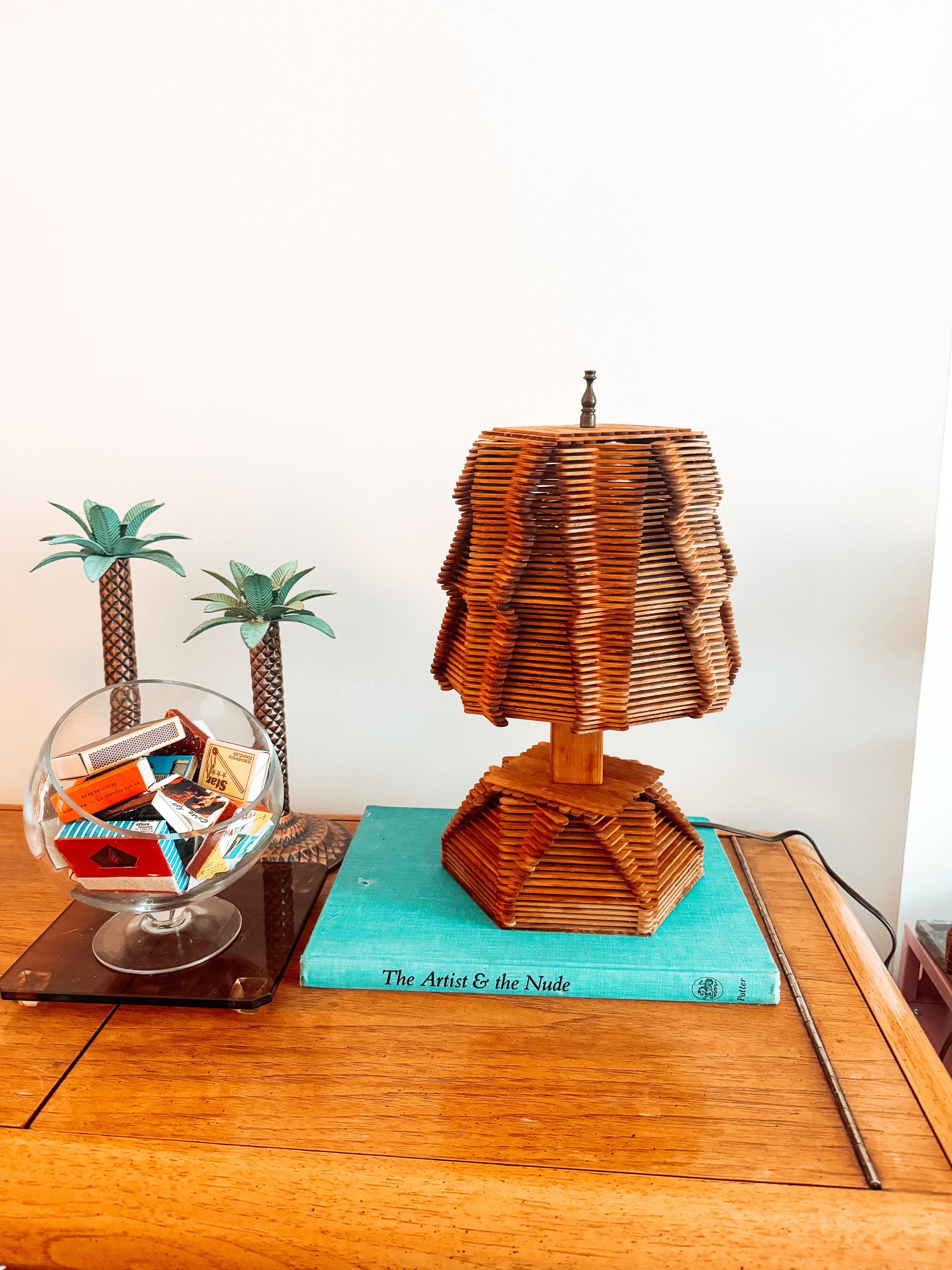 Captivating midcentury Folk Art table lamp is a remarkable representation of the post-war American hobby and craft movement. Handcrafted entirely from meticulously arranged popsicle sticks, the lamp showcases an intricate geometric design that