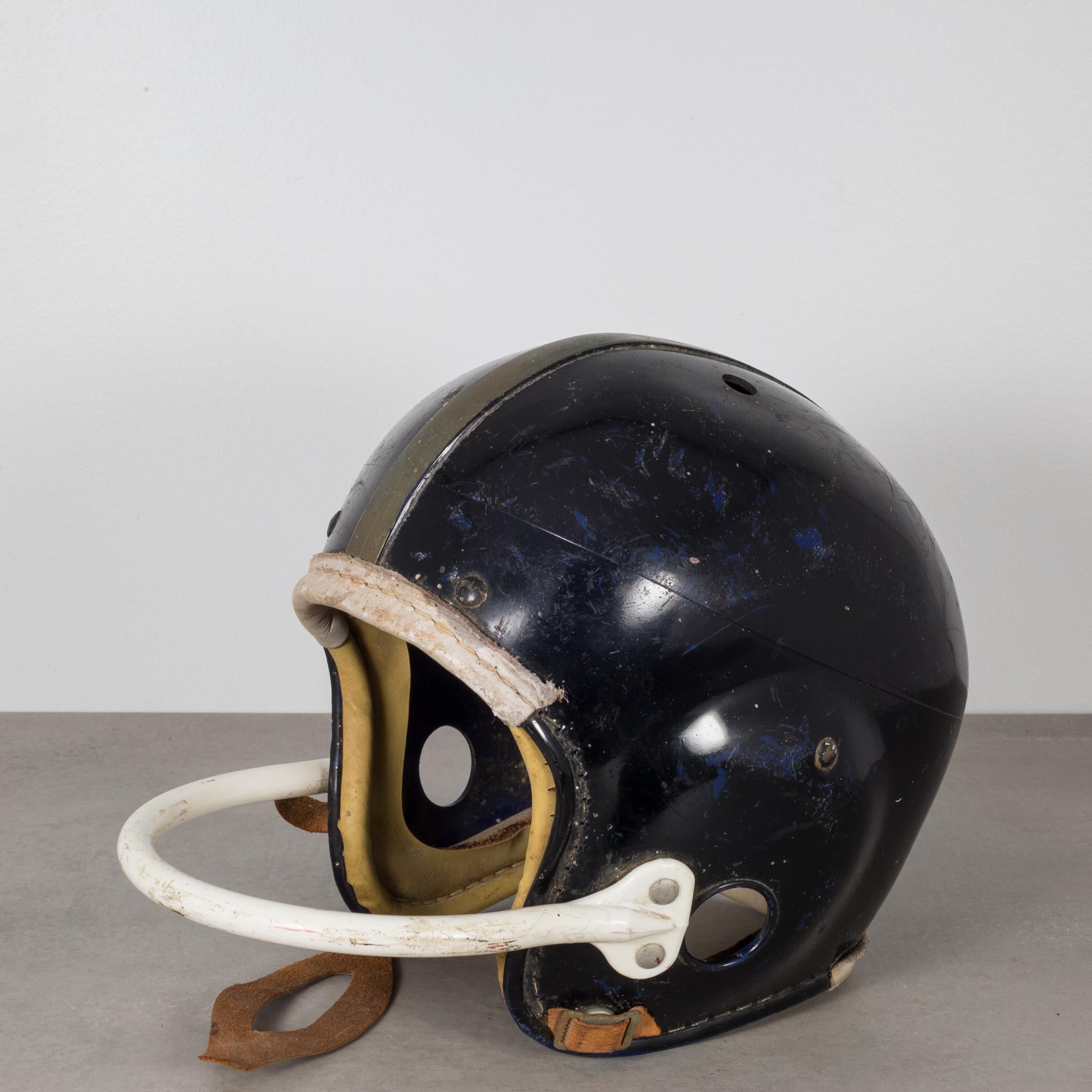 About
An original vintage football helmet with a single bar face mask. The helmet is black with a gold stripe running down the center, white face bar, leather chinstrap and leather cushion on the forehead and back of the head. There is a 
