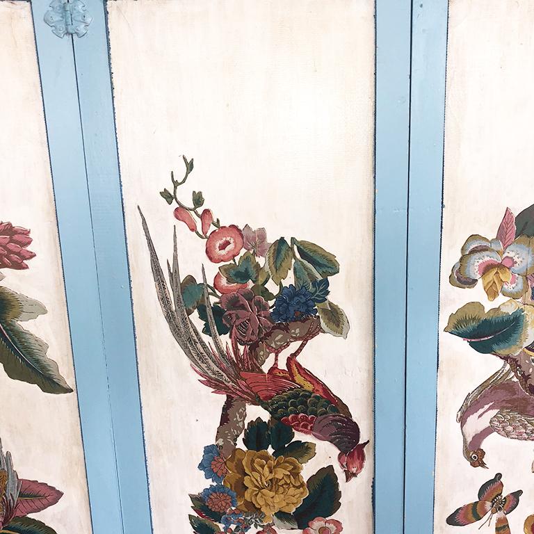Folding divider screen featuring colorful birds and flora on the front side. The back is upholstered in cloth and trimmed with intricate darker blue trim. Birds and floral on front are applied to wood on a cream background.

The outter corners of