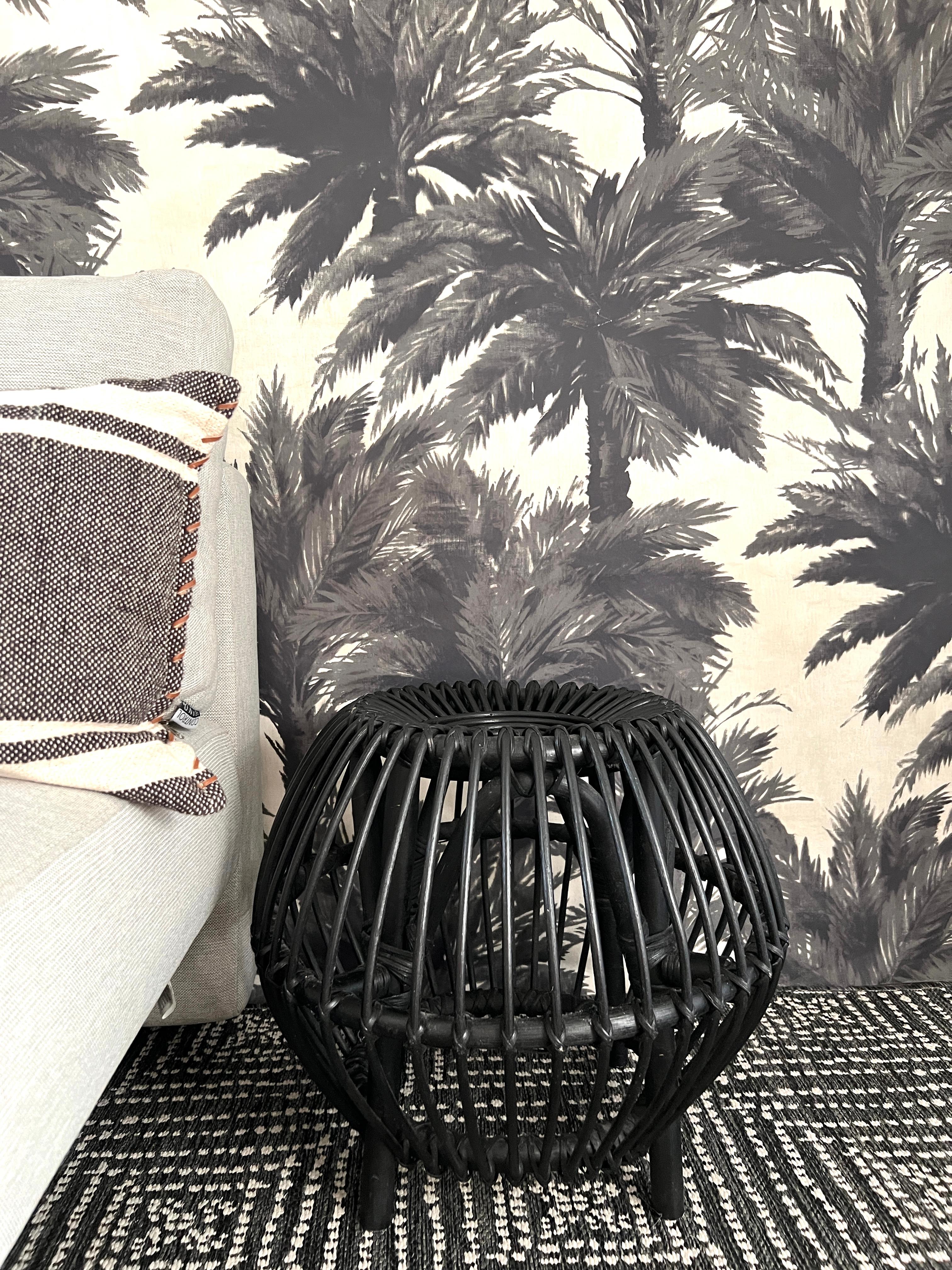 Hand-woven vintage ottoman in matte black rattan. The footed stool has a stylized round shape with organic open weave design. Versatile in functionality, this rustic item works as an ottoman, a side table, or as a design element in any room. Can be