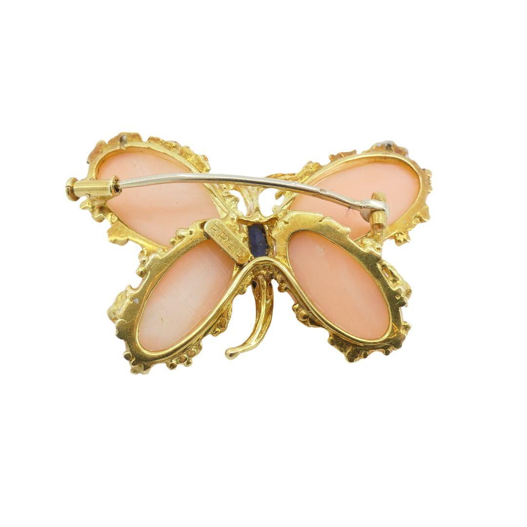 This vintage Fred Paris butterfly brooch from the 1970s is crafted from 18k gold and features a striking combination of Mediterranean coral and lapis lazuli. The wings are made of delicately light colored coral, while the body is crafted from lapis
