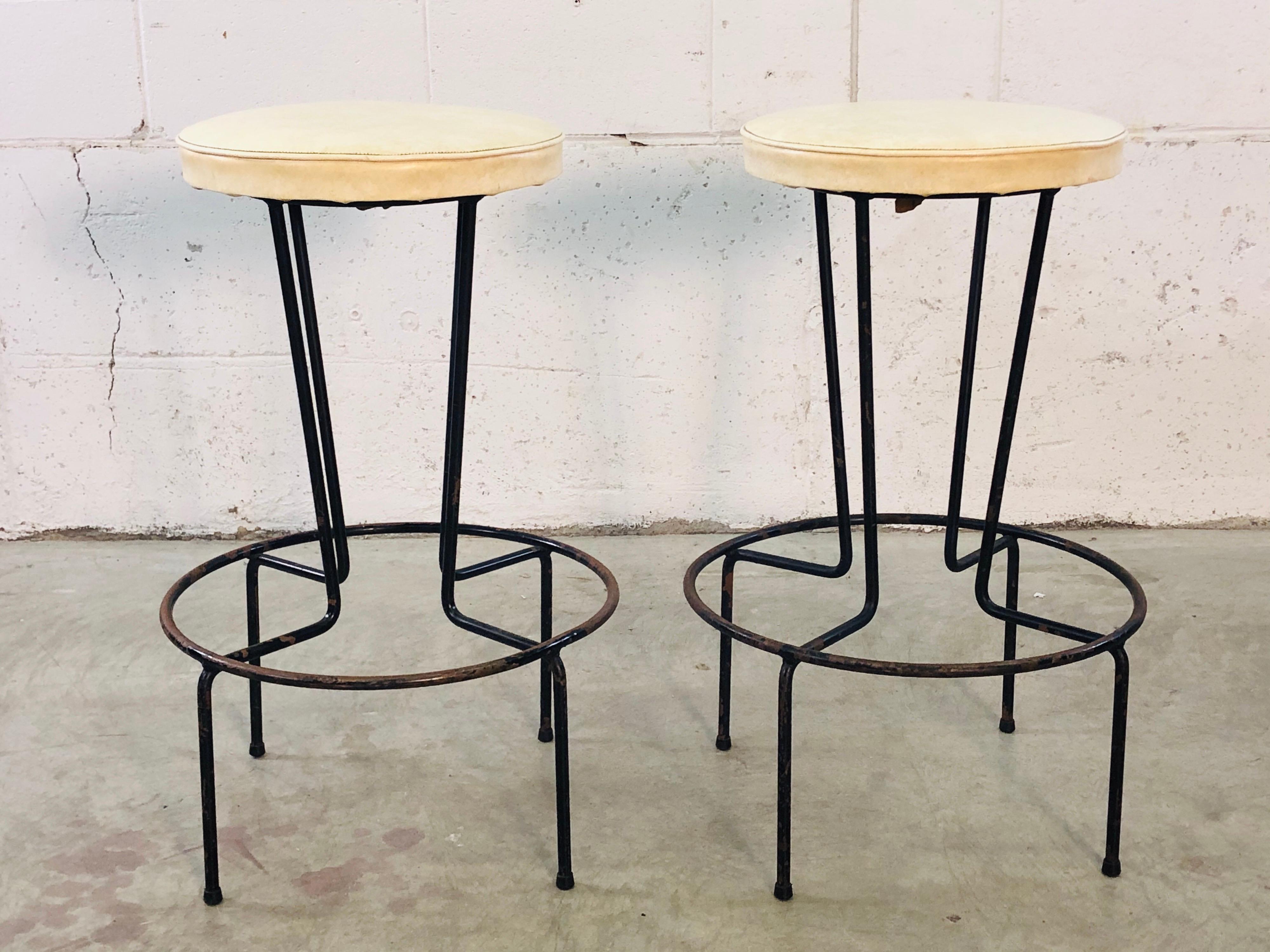 Vintage pair of Frederick Weinberg wrought iron stools with the original vinyl seats. The stools have a round accented base and the bases are in original condition. One stool has a very small split in the vinyl. Does not appear to go all the way