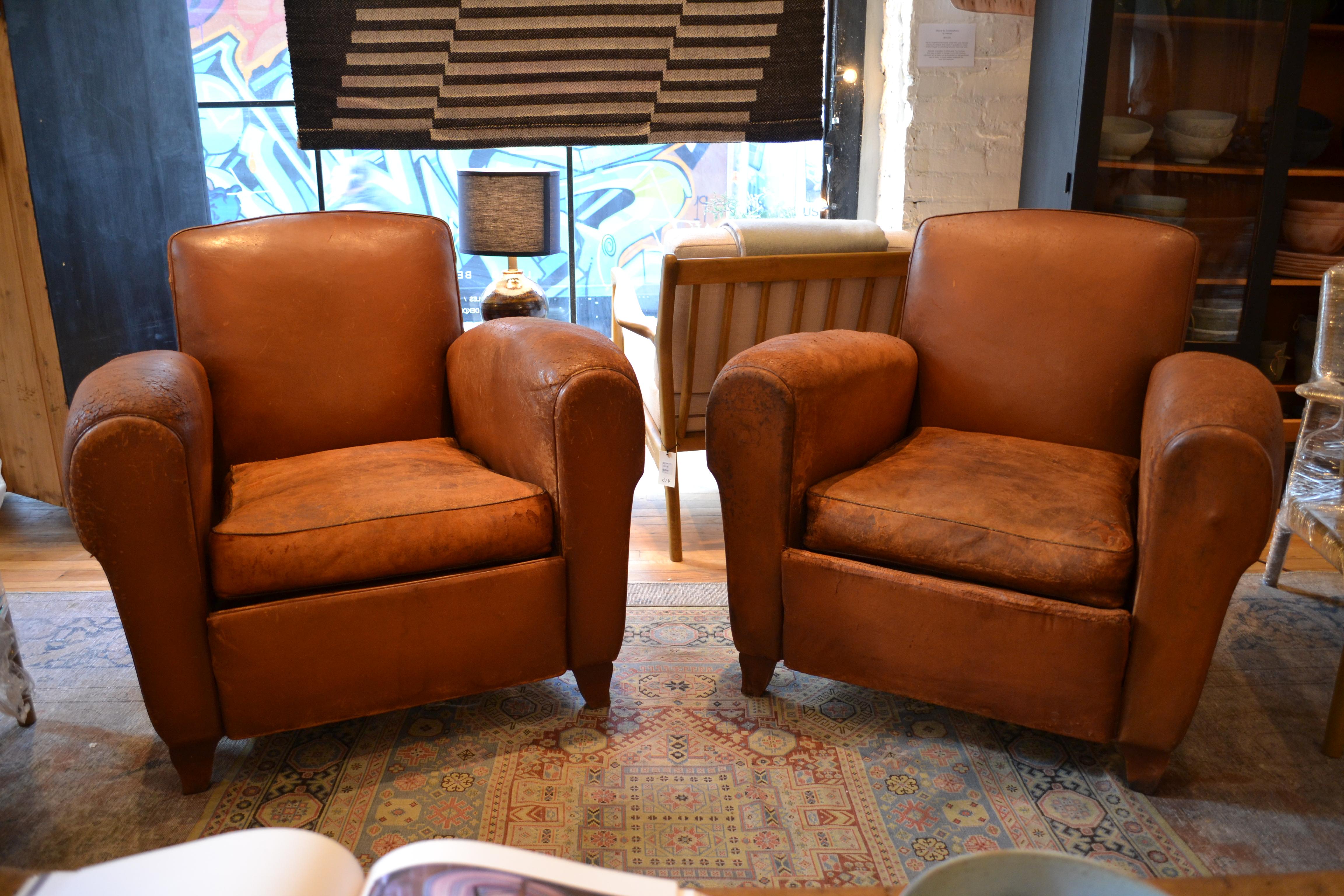 Beautiful French leather club chairs. A design staple, the comfortable and classic French club chair is a timeless piece and this pair is no exception. High arms and shallow back make these chairs inviting and homey. The perfect duo to add warmth to