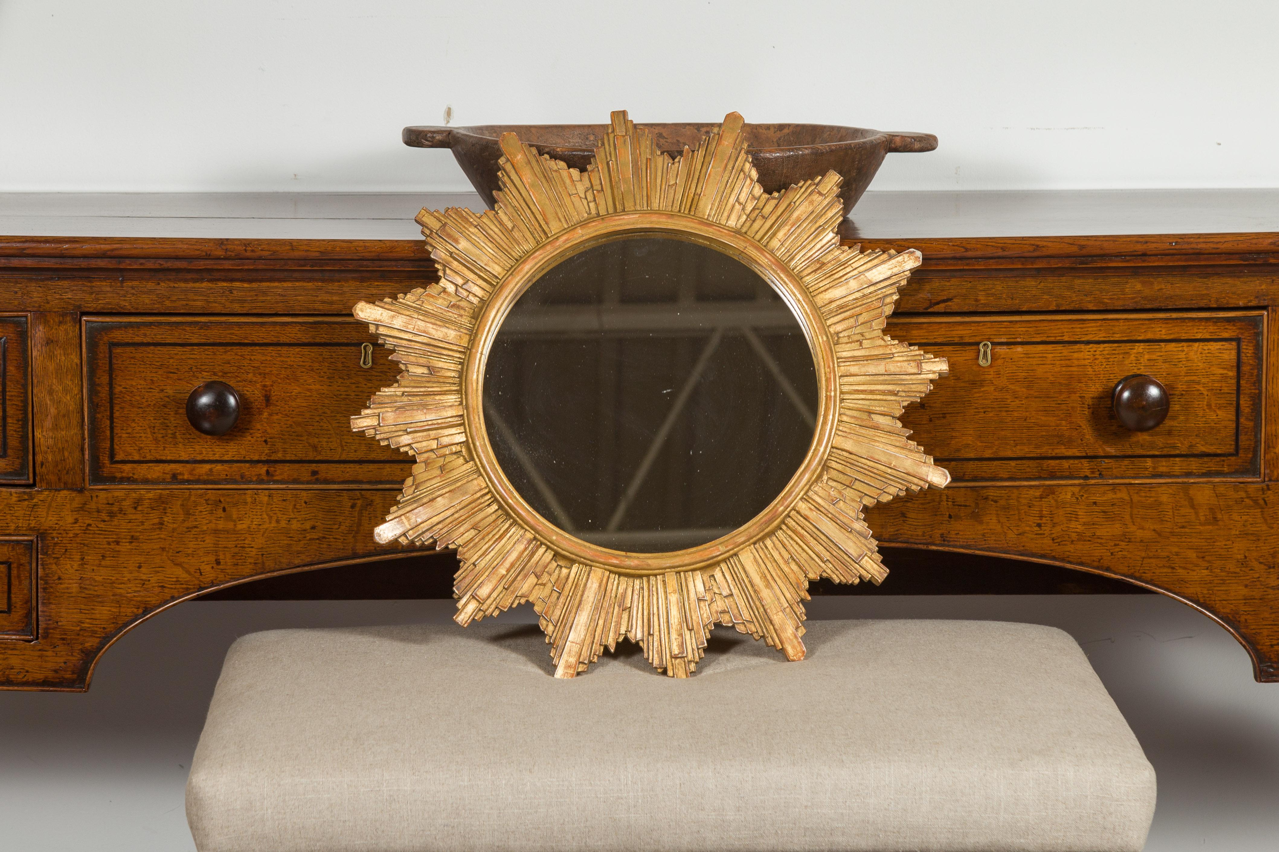 A French vintage gilt composition sunburst from the late 20th century, with rays of varying sizes and flat mirror. Born in France during the 1970s, this sunburst features a clear mirror plate surrounded by a molded inner frame, from which are