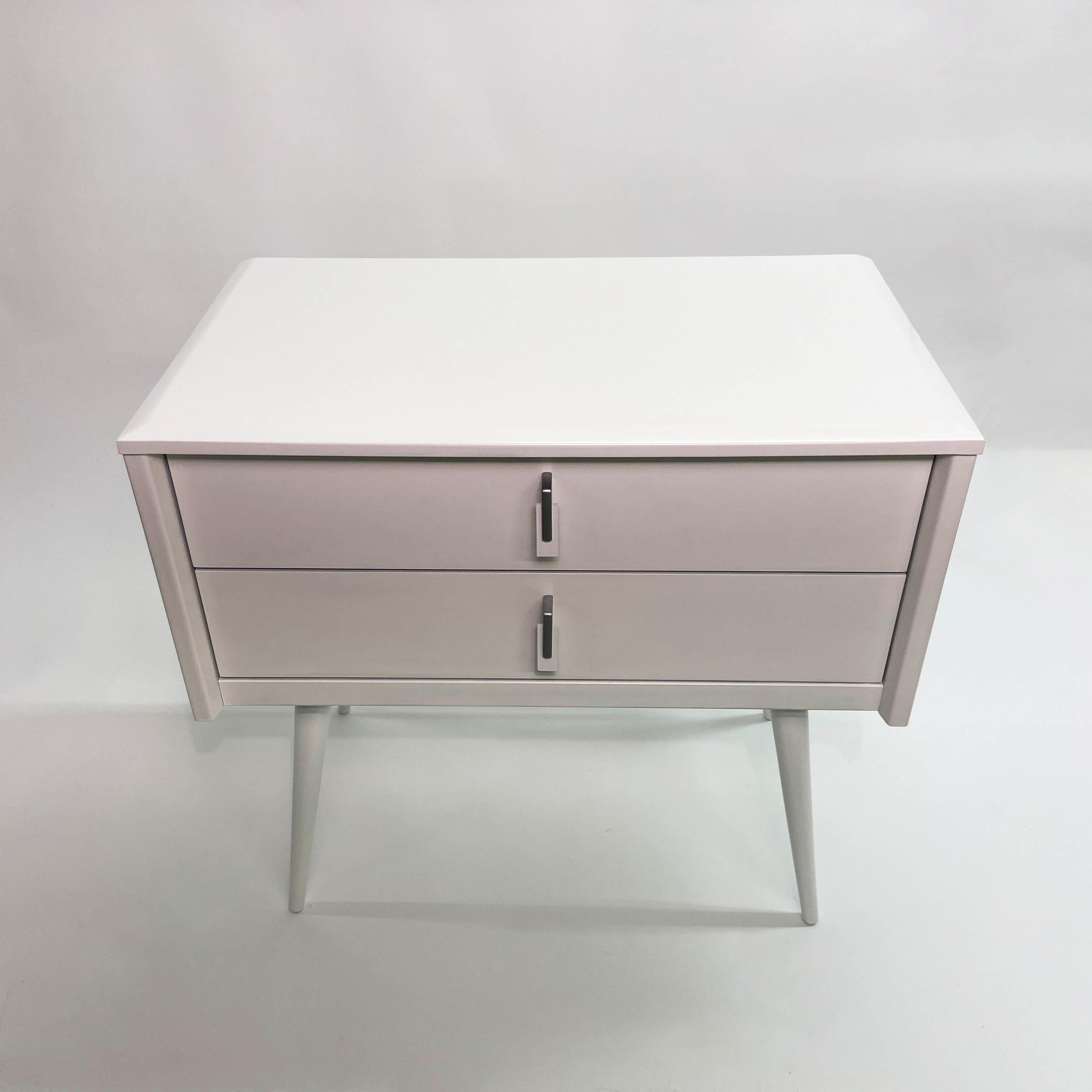 Offering a sleek and stylish French Mid-Century Modern double drawer nightstand or end table. It has been newly refinished in Dove White lacquer. This vintage piece is made in France by Gautier and edited by Montage using original Paul McCobb legs