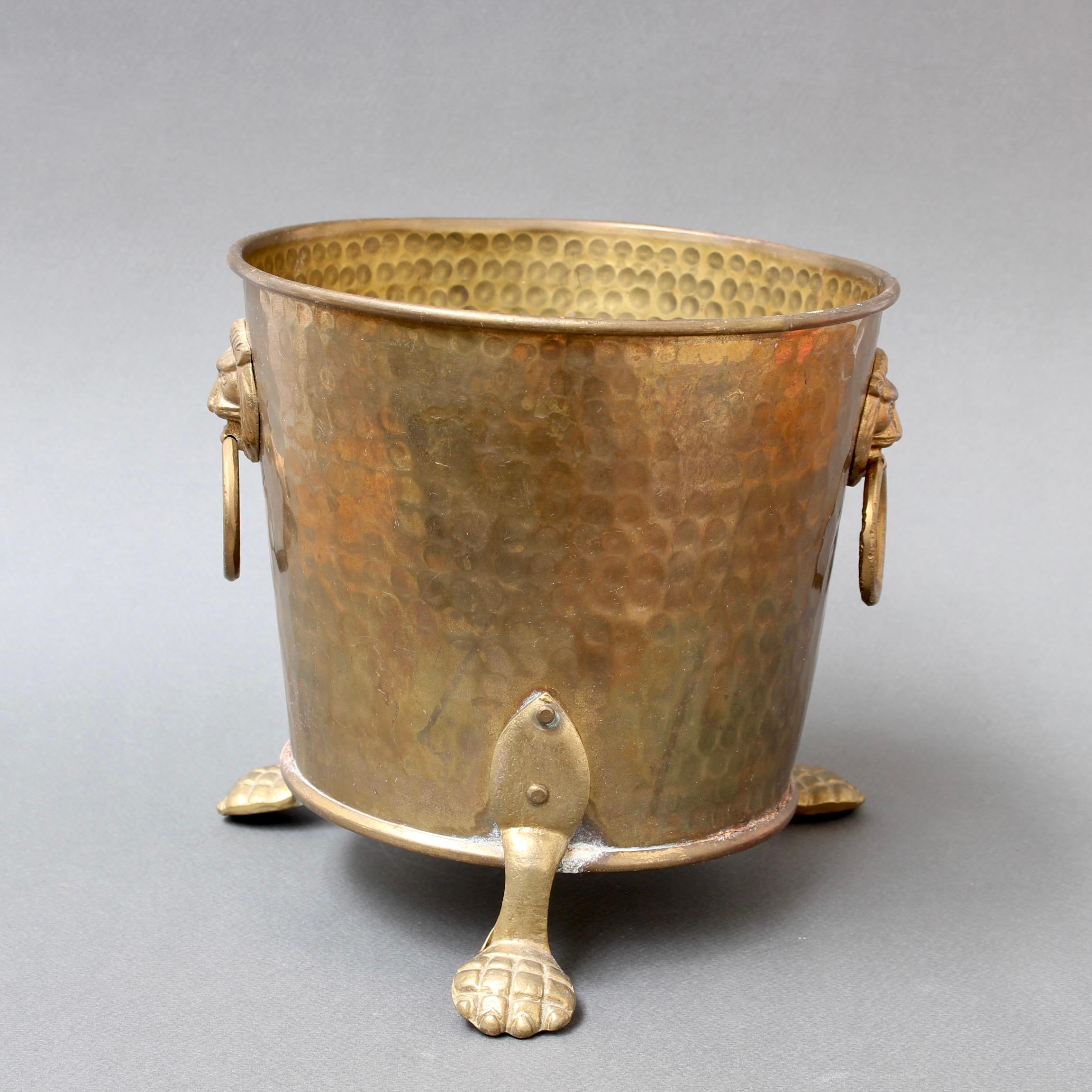 Vintage 3-legged French brass ice bucket or cachepot (circa 1930s). Lion motif handles with rings on two sides accent this wonderful vintage piece with three monopodium (animal paw) style feet. The piece was originally intended to be used as a