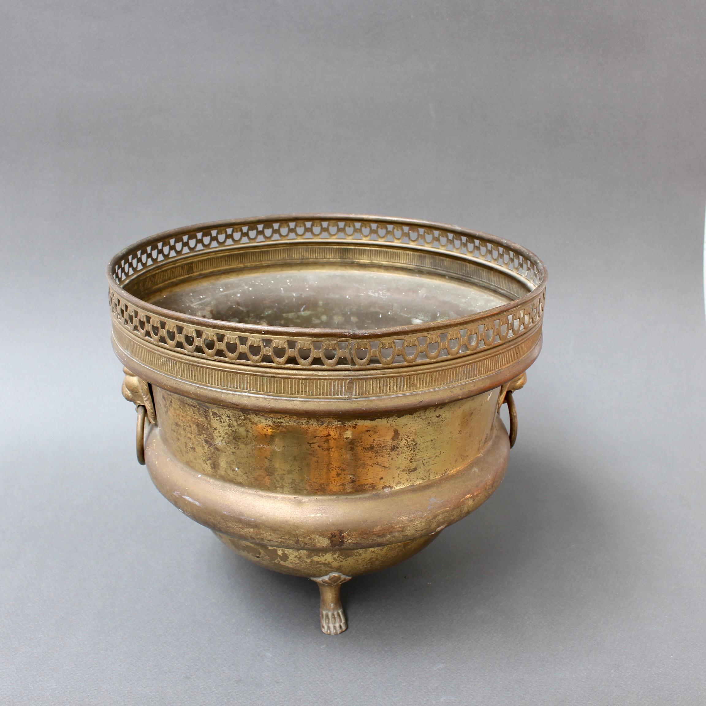 Vintage 3-legged French brass ice bucket or cachepot (circa 1940s). Lion motif handles with rings on two sides accent this wonderful vintage piece with three monopodium (animal paw) style feet. The piece was originally intended to be used as an ice