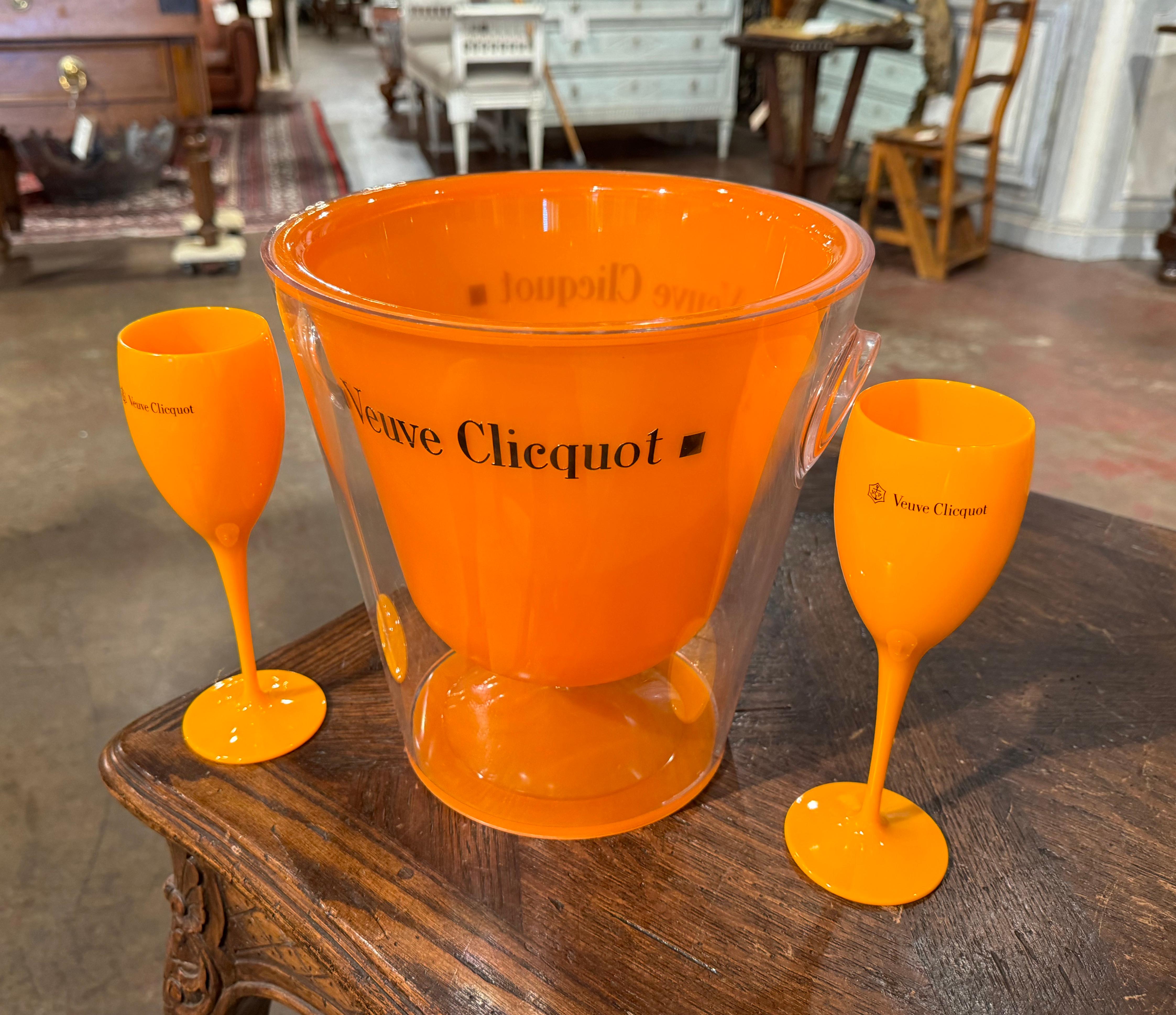 Decorate a wet bar with this elegant champagne bucket with two matching glasses. Crafted in France circa 1980 by the iconic House of Veuve Clicquot, the acrylic cooler is decorated with the company's insignia. The bucket and the two flutes are in