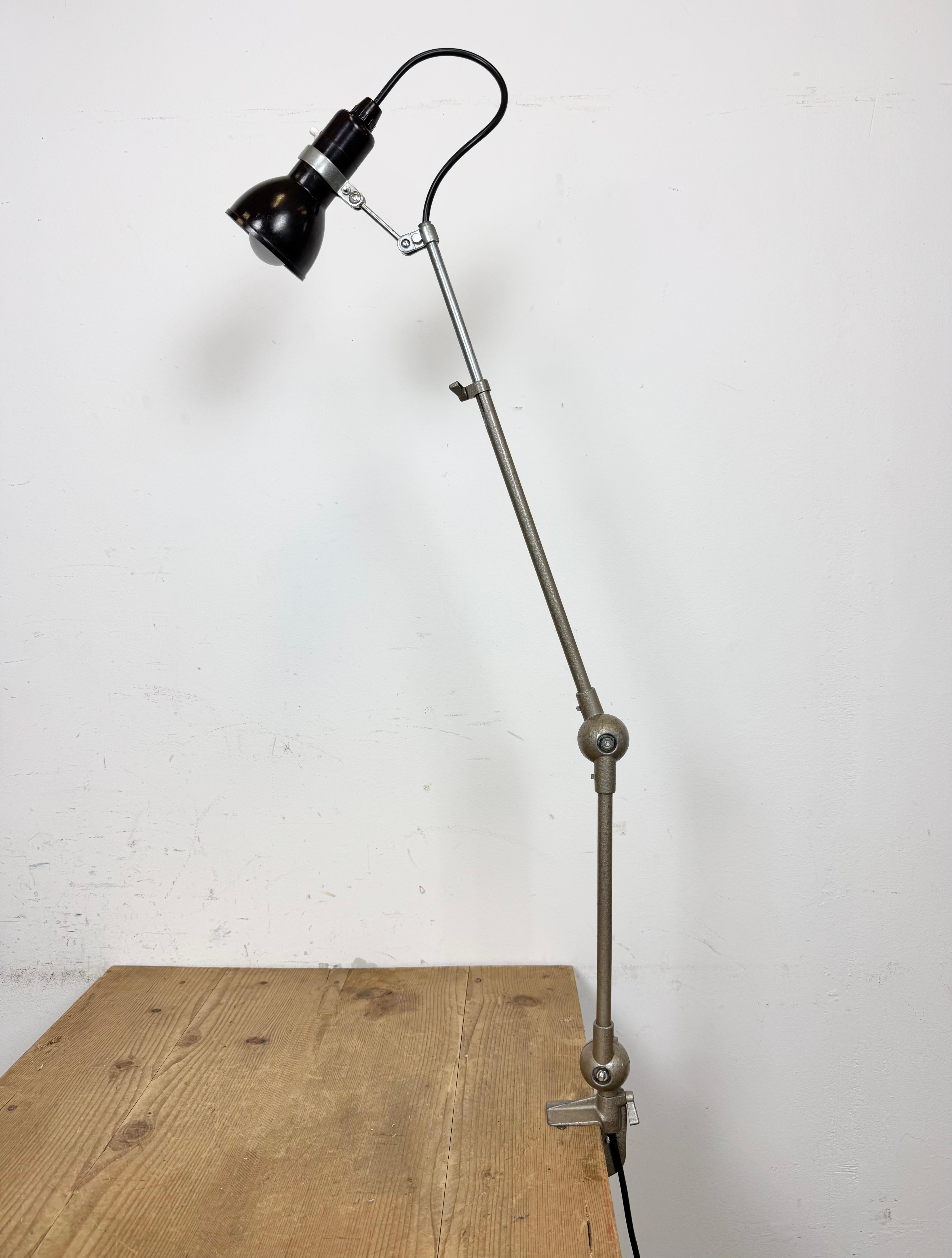 Lámpara de sobremesa vintage de taller, de color gris martillado, regulable en altura y ángulo, fabricada en Francia en 1960. Tiene una pantalla de baquelita marrón con interruptor, un brazo de hierro y una base de pinza.  Bombillas E14. Cable