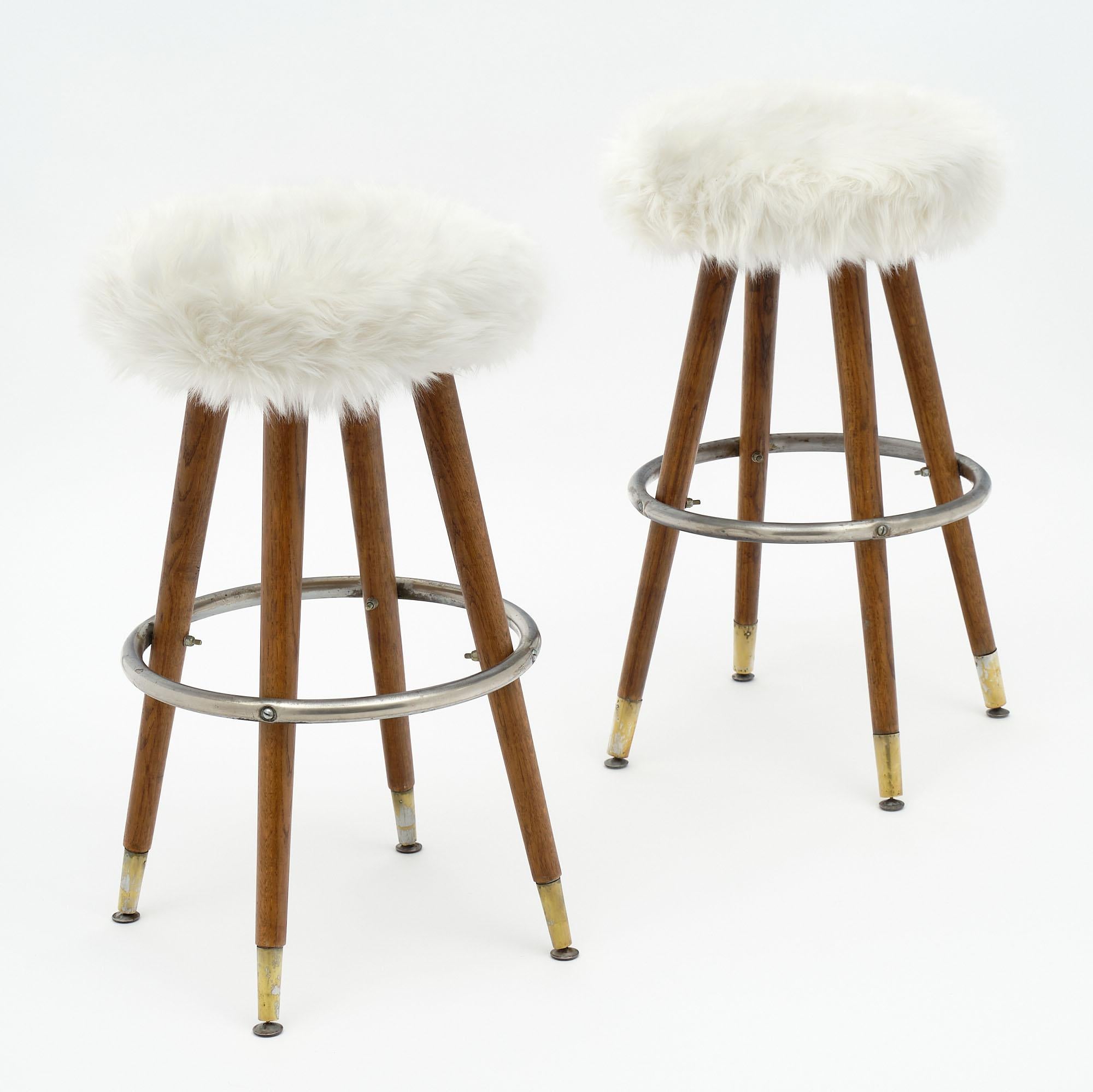 Bar stools, French, made of solid beech wood tapered legs, and steel circular foot rests. They have solid brass feet. The stools are covered with a new ivory shag upholstery fabric. The diameter of the seat is approximately 16.5”.