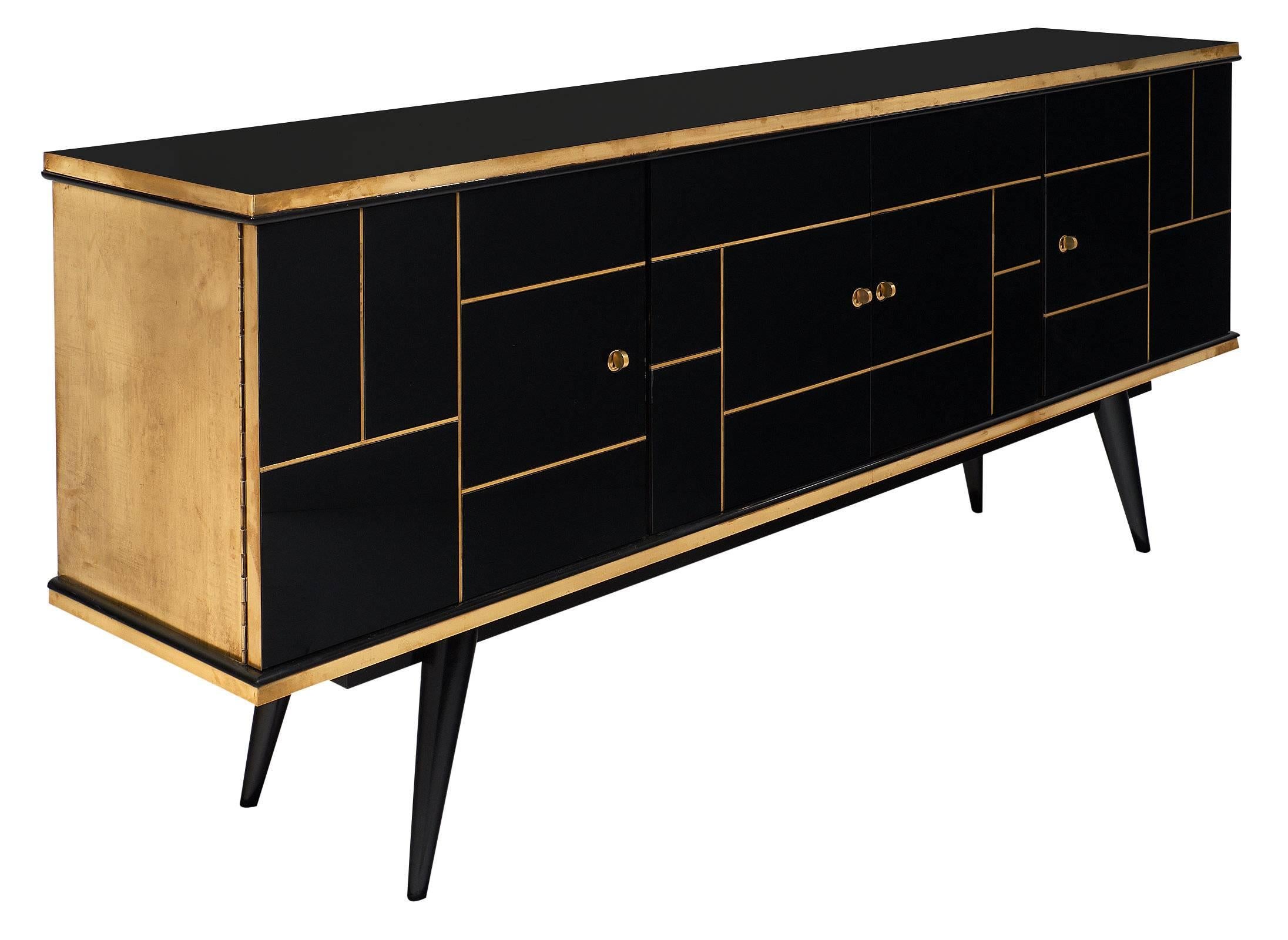 A fine French Modernist credenza customized with black glass panels trimmed in brass on its facade. The piece has full brass side panels and trims. Four doors open to a pristine satin wood interior. Four tapered legs flare out to support the buffet.