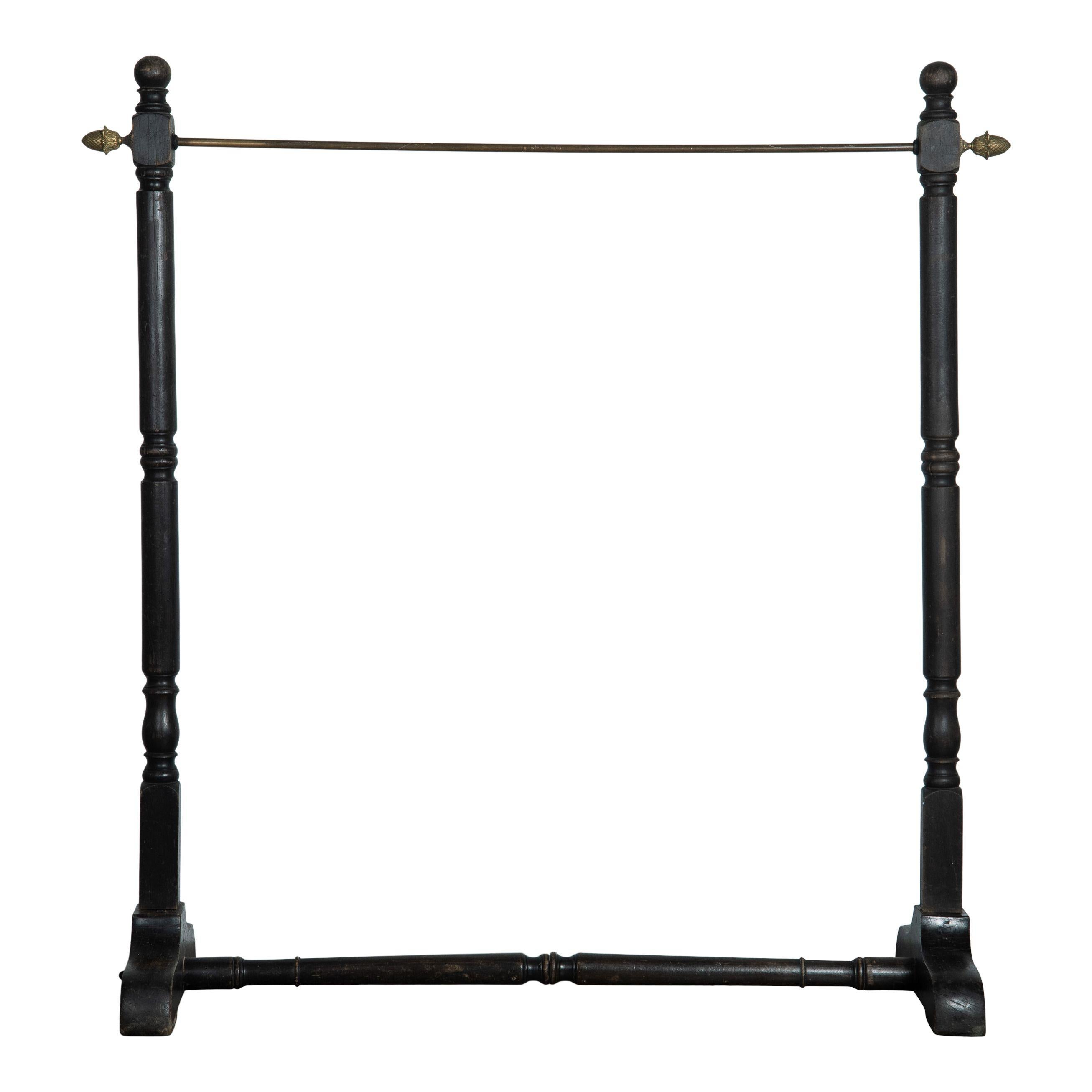 Vintage black wood clothing rack from France. This clothing rack has a simple design with a metal bar for hangers that features gold metal adornments on each side that resemble acorns. The simple legs are a carved wood and are finished with a simple